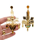 All gold Festive drop statement earrings shown hanging against a white background with my hand behind for scale.