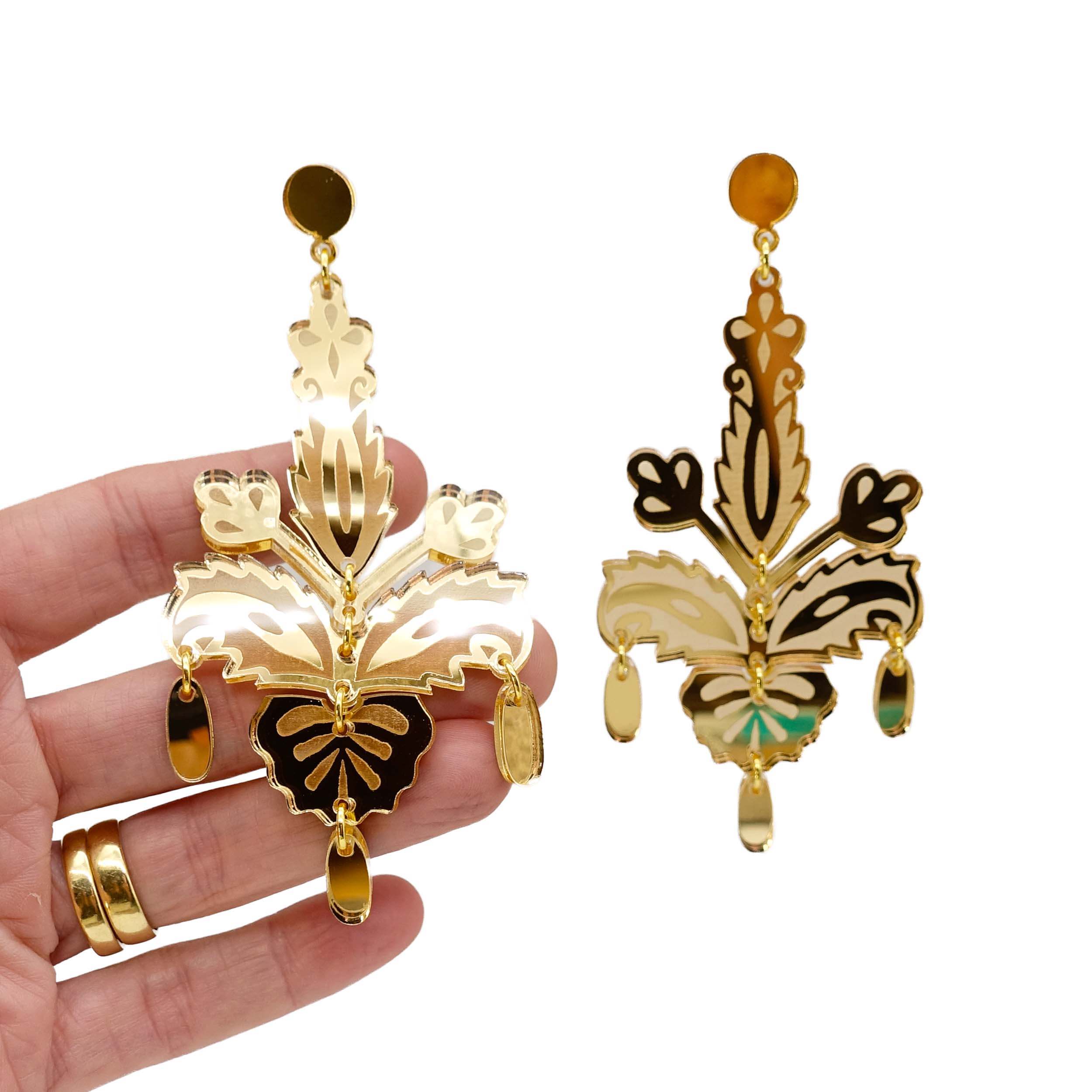 All gold Festive drop statement earrings shown hanging against a white background with my hand behind for scale.