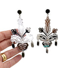 Silver Festive Drop statement earrings shown hanging against a white background with my hand behind for scale.