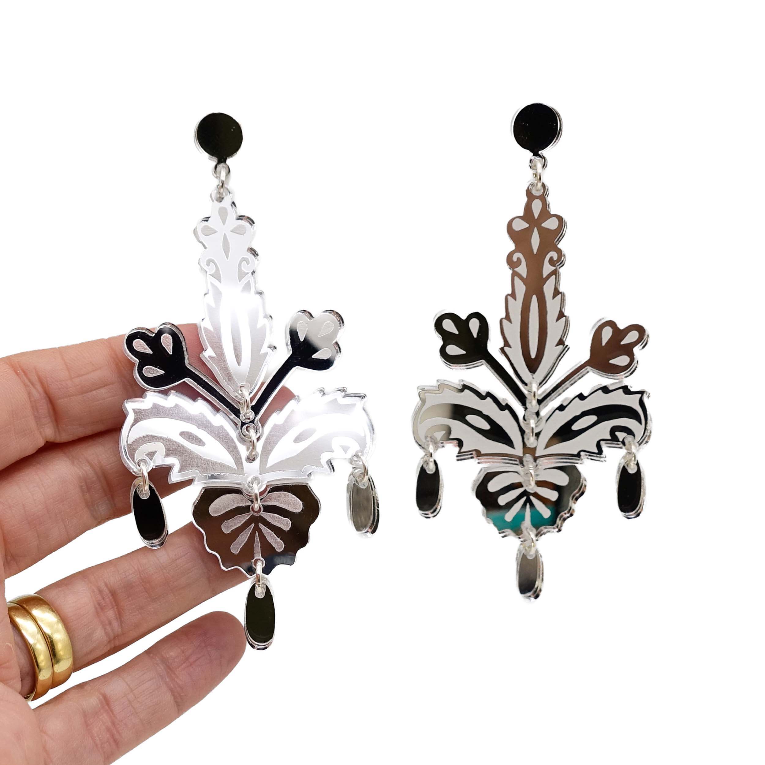 Silver Festive Drop statement earrings shown hanging against a white background with my hand behind for scale.
