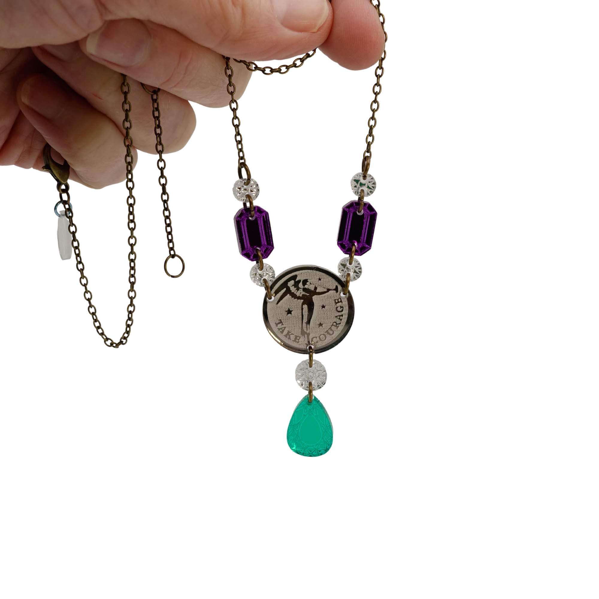 A necklace with a bronze coin shaped centerpiece etched with Sylvia Pankhurst's Angel of Freedom and Christabel Pankhurst's words, 'Take Courage,' with purple and green acrylic jewels in the style of the original Suffragette jewellery.