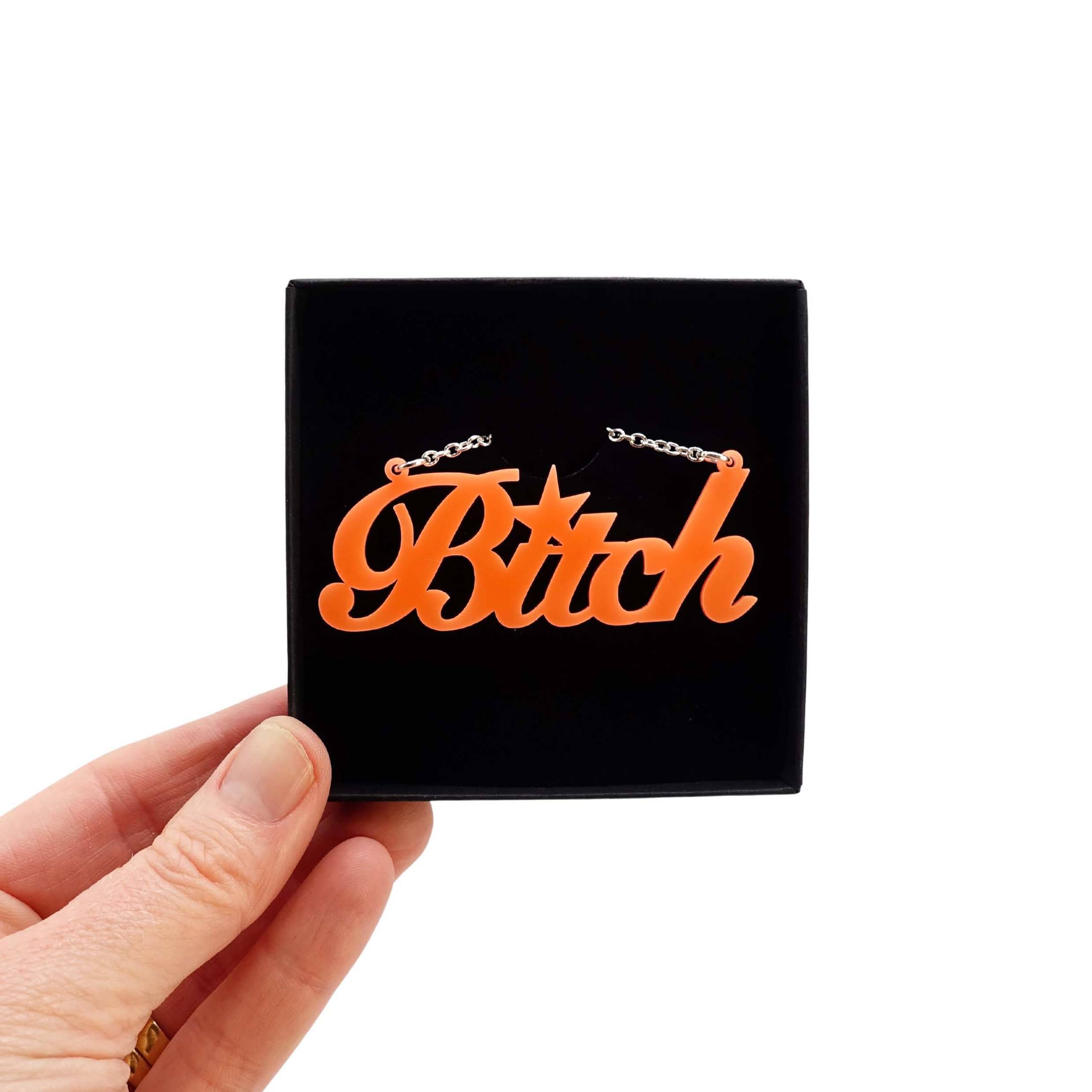 B*tch necklace in day-glo orange shown held up in a Wear and Resist box. £2 goes to Bloody Good Period.