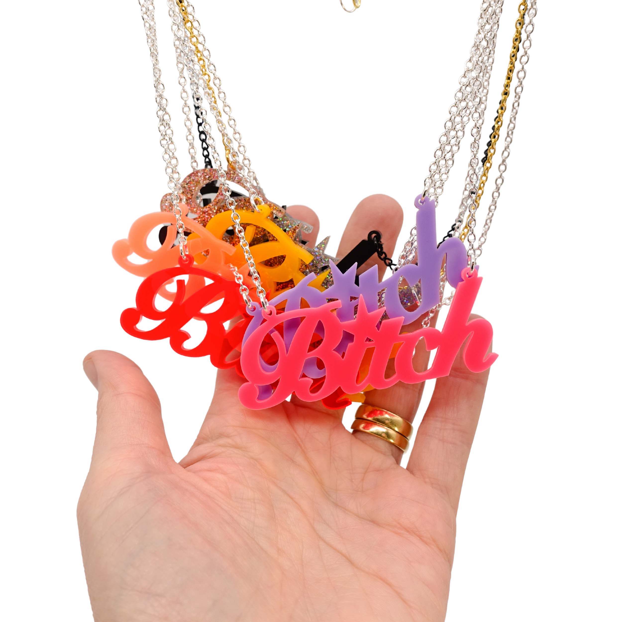 My hand behind a group of B*tch necklaces all hanging together.