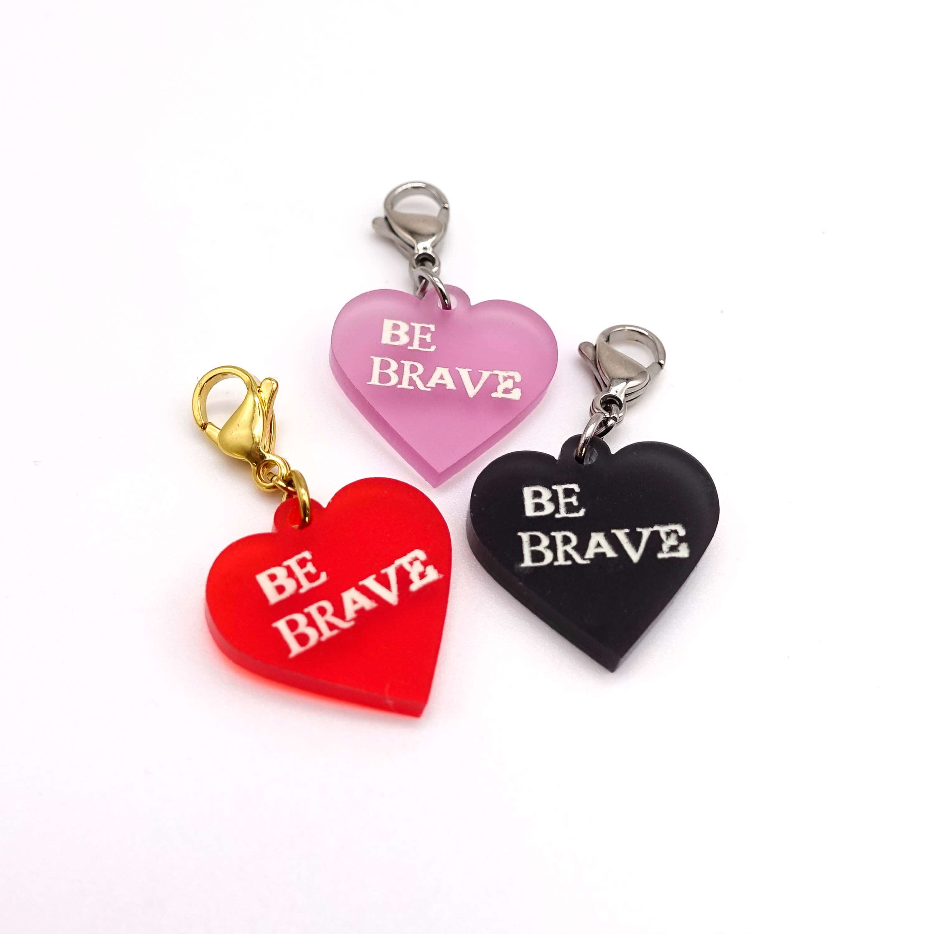Heart charms in chilli frost, pink frost and slate frost etched in glow-in-the-dark pigment with the words 'Be Brave'