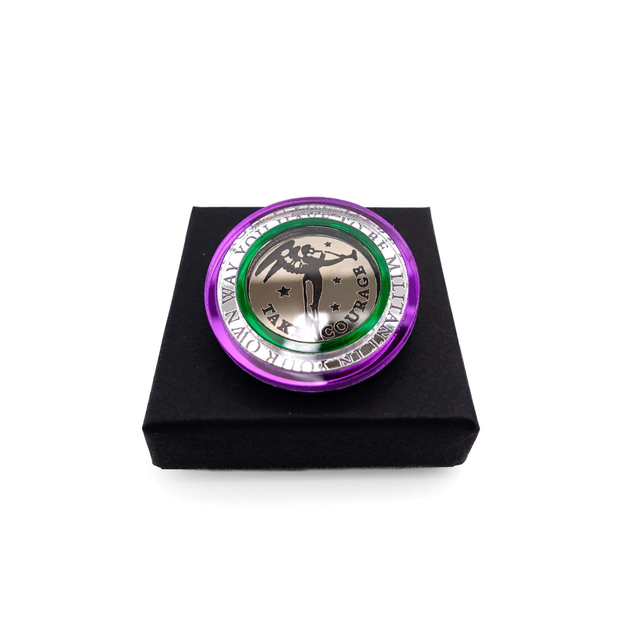 A round brooch etched with the words You have to be militant in  your own way, from Emmeline Pankhurst's famous quote. The centre is a bronze etched Angel of Freedom by Sylvia Pankhurst with stars and the bands surrounding it are in the Suffragette colours.