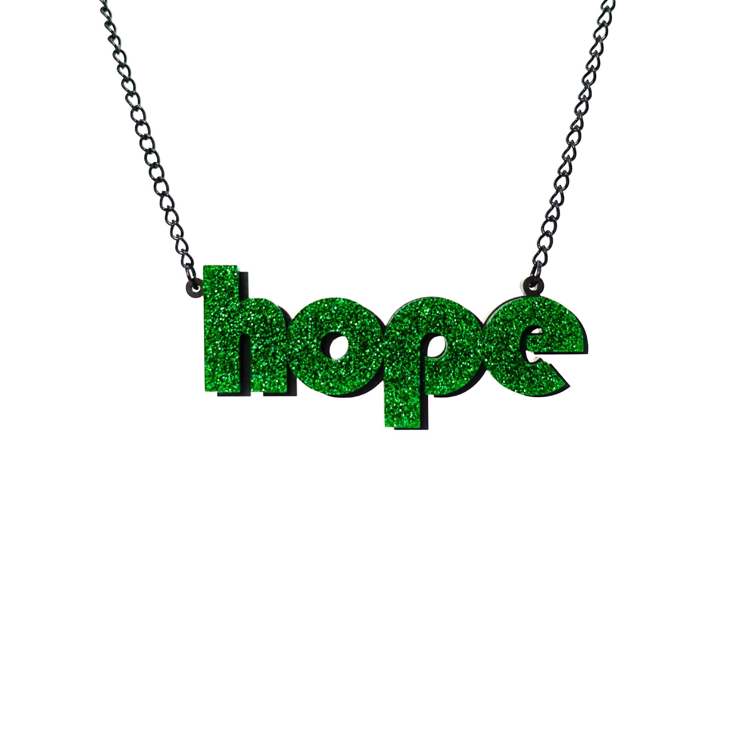 Hope statement necklace in green glitter with backing layer that works as a drop shadow, shown hanging against a white background. £2 goes to Women for Refugee Women charity.