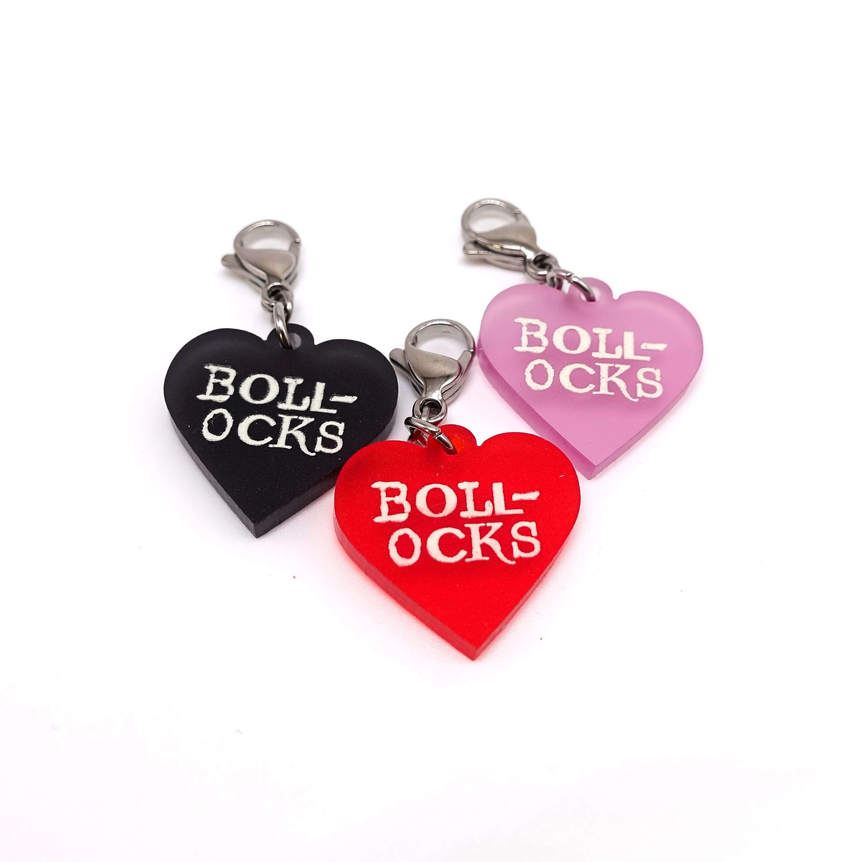 Heart charms in chilli frost, pink frost and slate frost etched in glow-in-the-dark pigment with the word 'Bollocks'