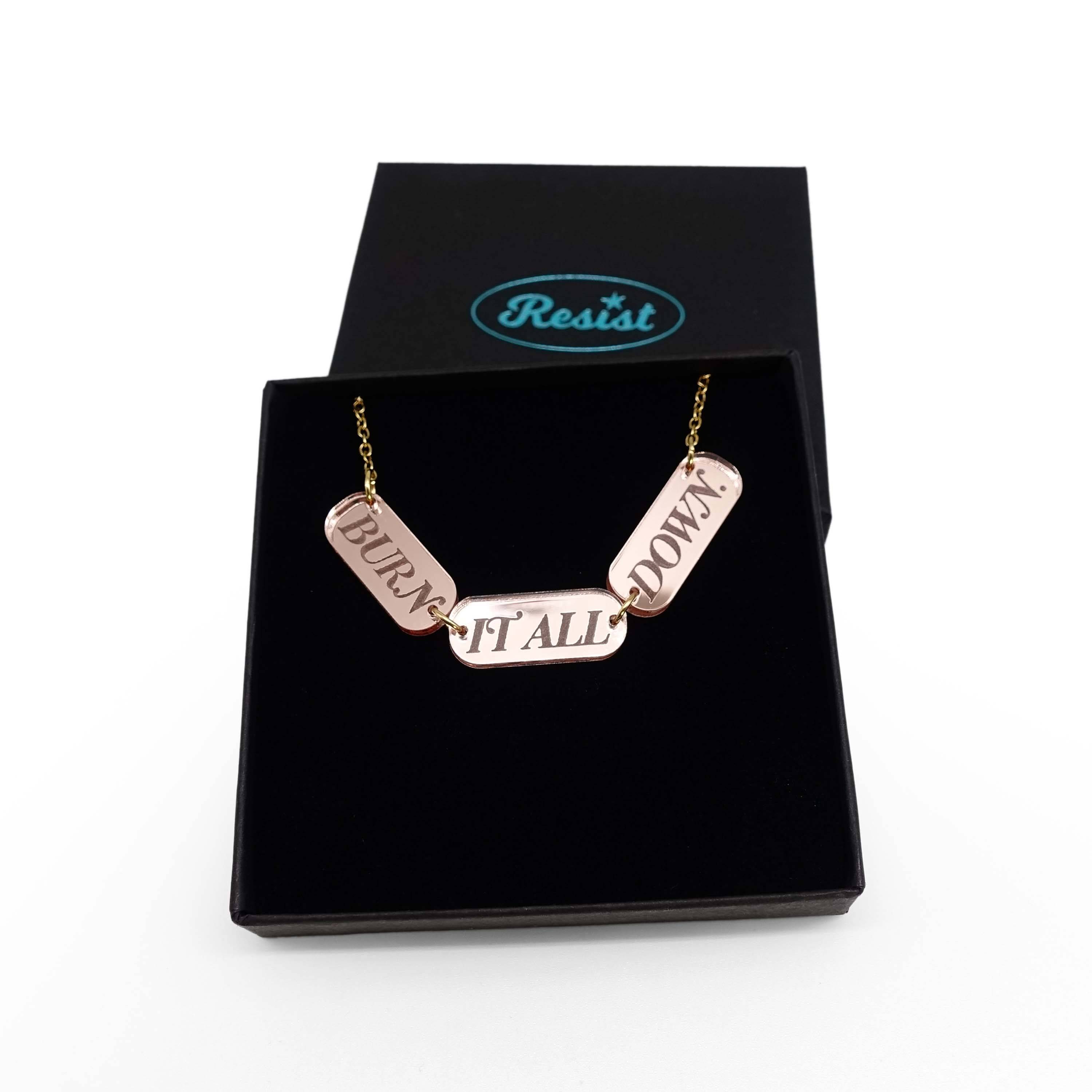 The BURN IT ALL DOWN necklace in rose-gold mirror on a gold-plated stainless steel chain, shown in a Wear and Resist gift box.