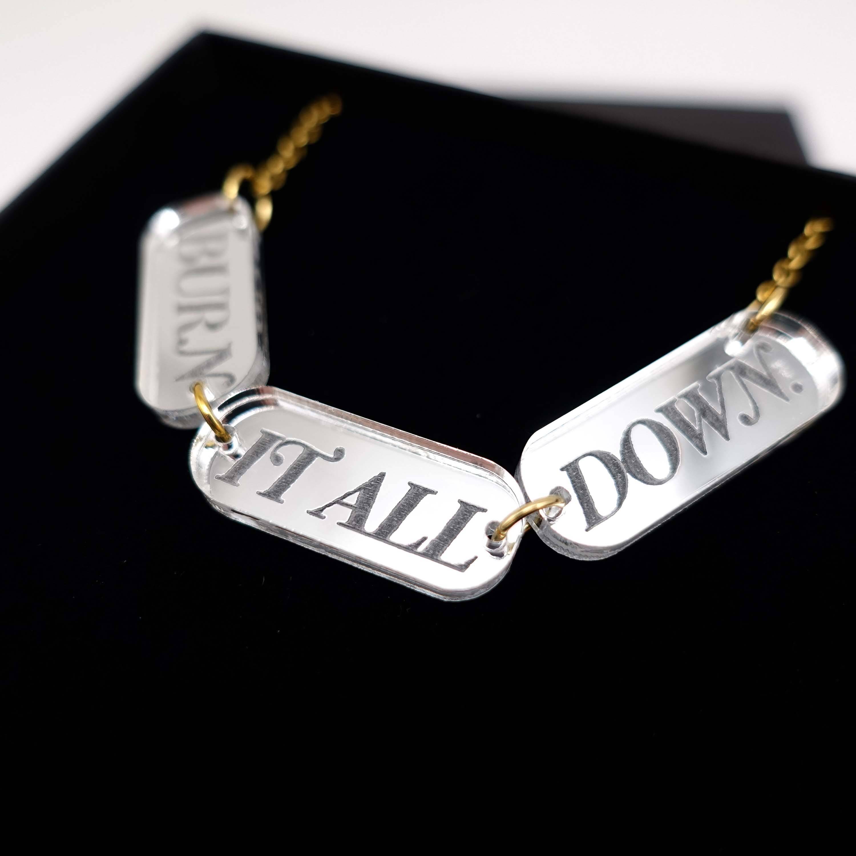 The BURN IT ALL DOWN necklace in silver mirror on a gold-plated stainless steel chain, shown in a Wear and Resist gift box.
