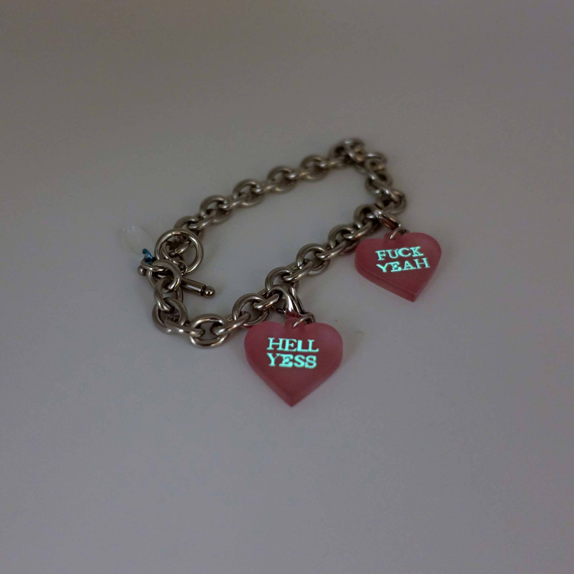 Stainless steel charm bracelet with pale pink Hell Yes and F*ck Yeah heart charms glowing in the dark.