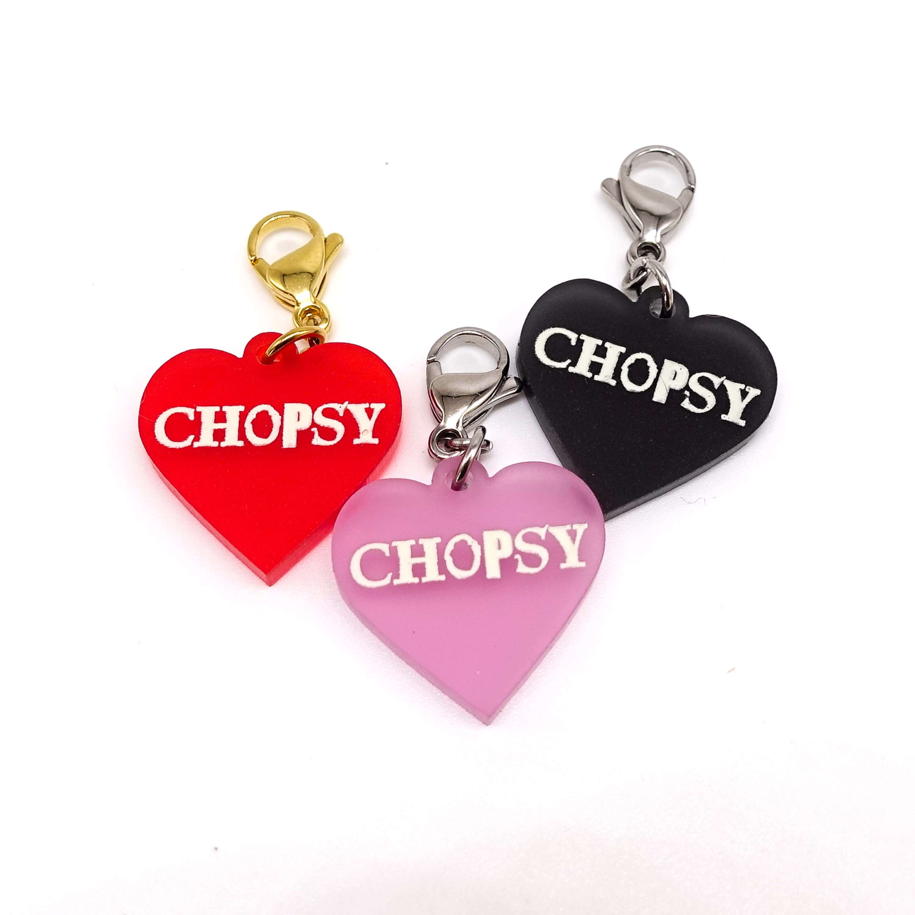 Heart charms in chilli frost, pink frost and slate frost etched in glow-in-the-dark pigment with the word 'Chopsy'