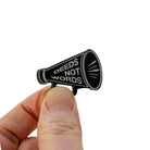 A small megaphone brooched etched with 'Deeds not words' shown held up for scale against a white background.
