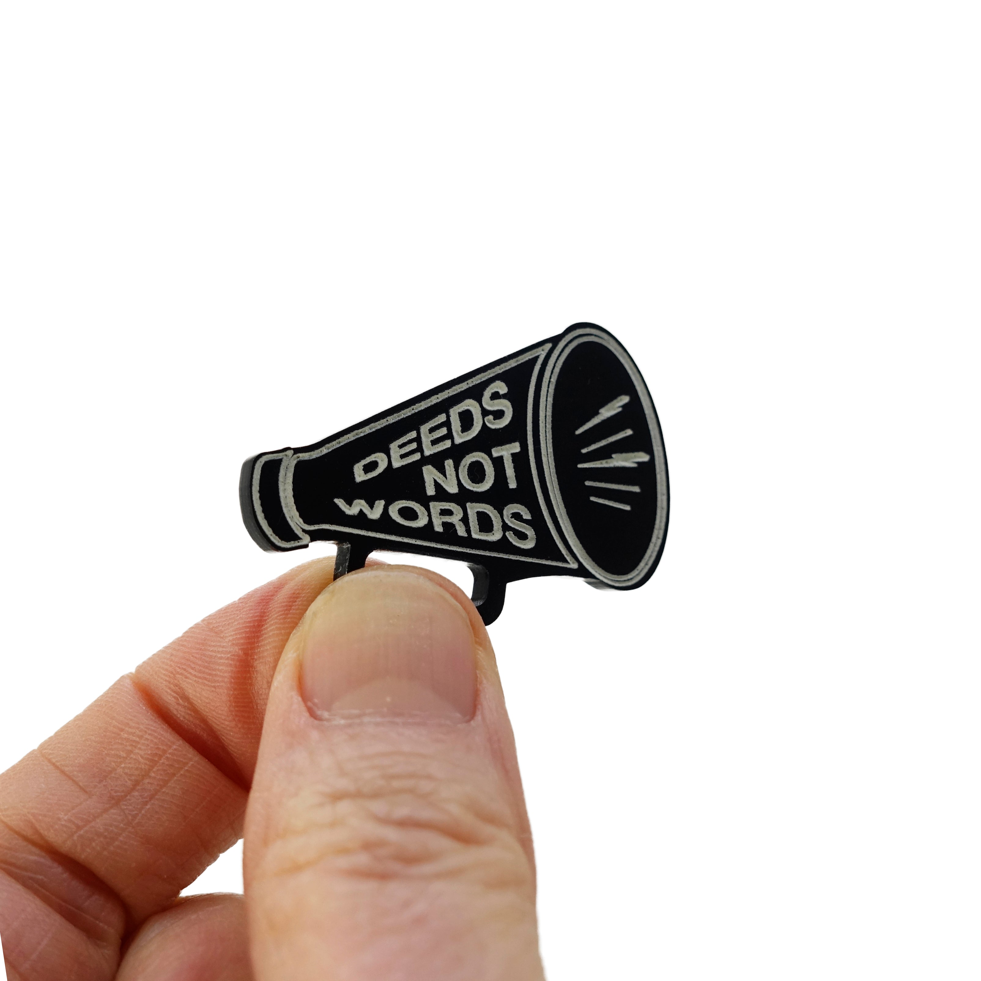A small megaphone brooched etched with 'Deeds not words' shown held up for scale against a white background.