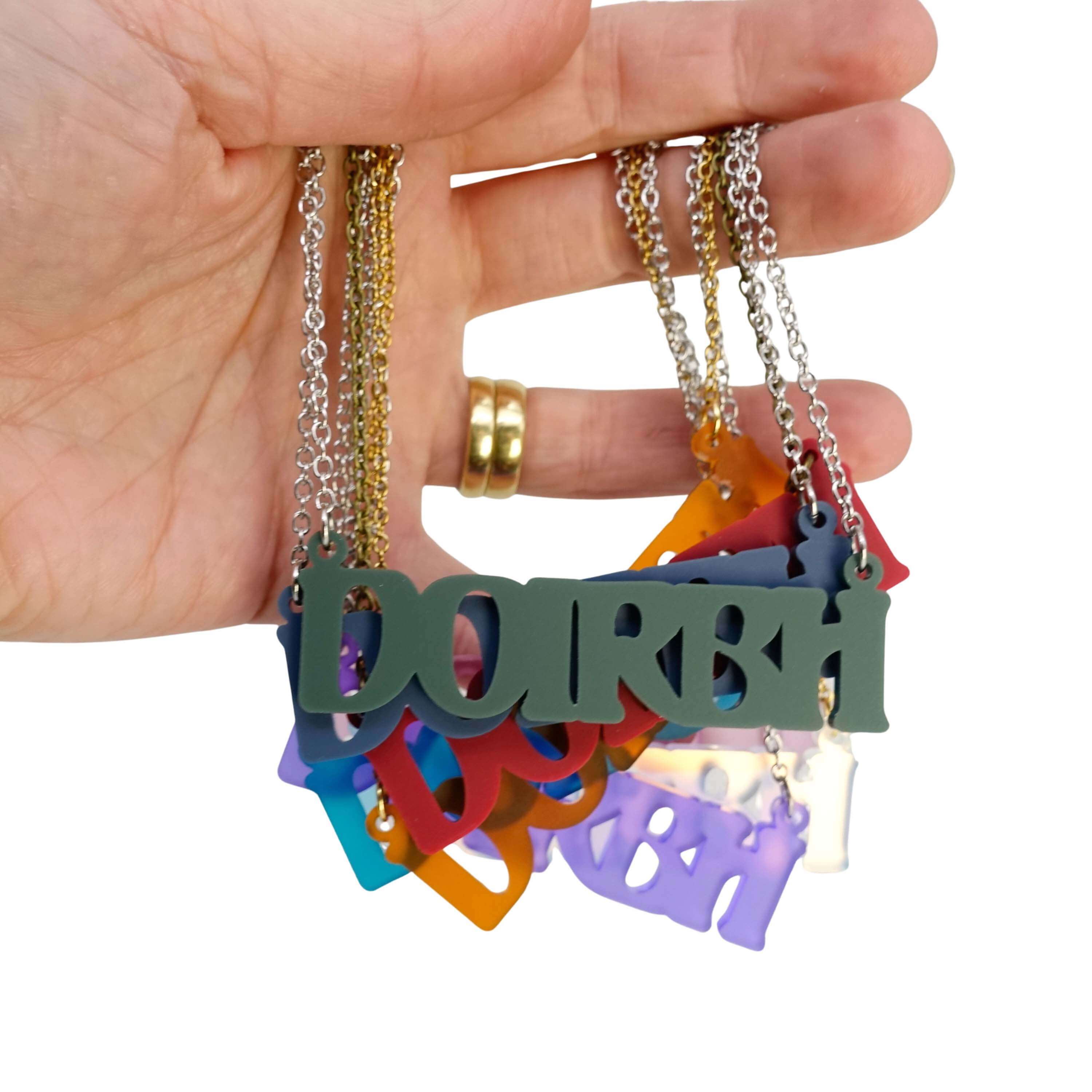 My hand holding all of the different colours of DOIRBH Gaelige necklace for Irish difficult women, with matte moss at the front.