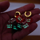 My hand holding the *ck This huggie hoop earrings glowing in the dark.