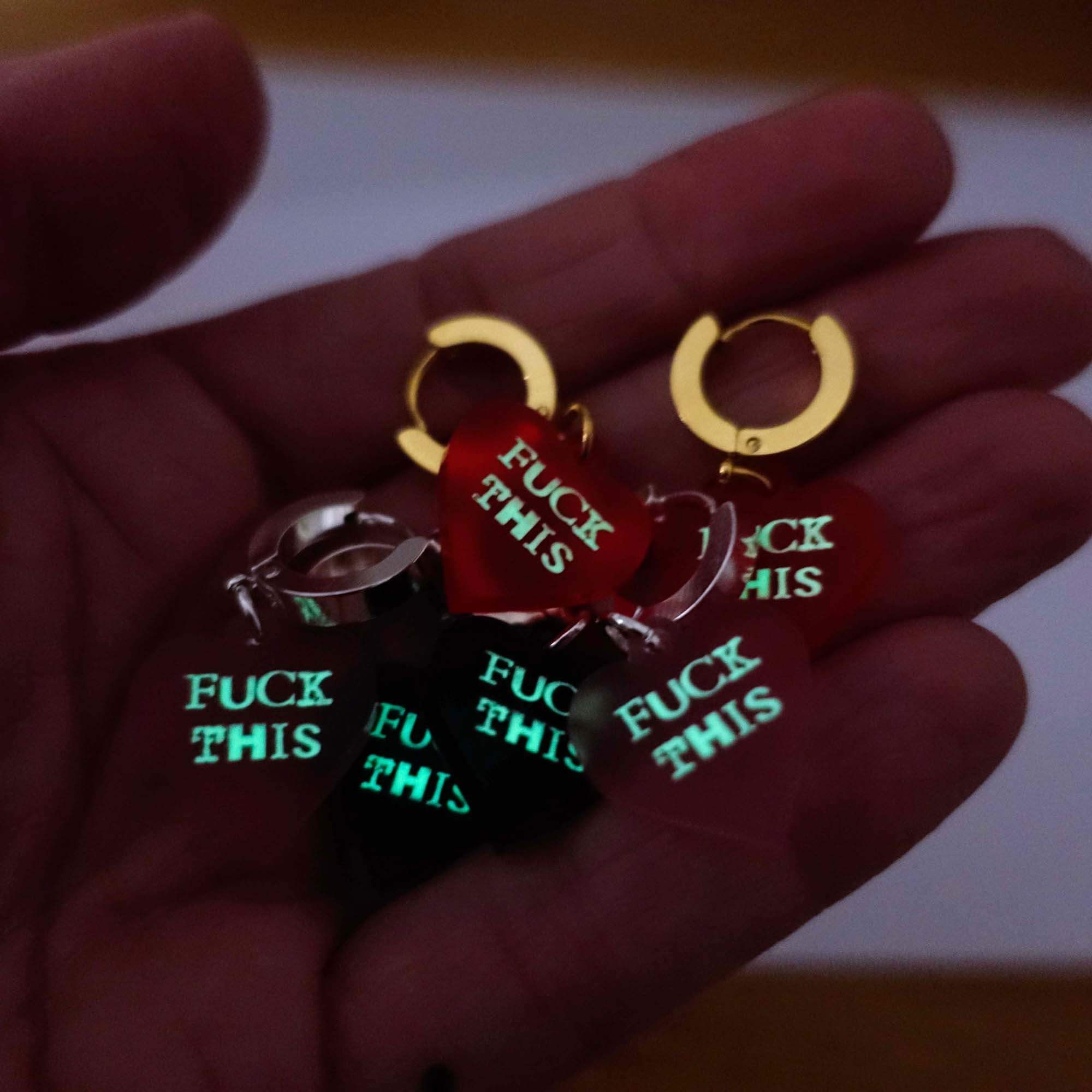 My hand holding the *ck This huggie hoop earrings glowing in the dark.