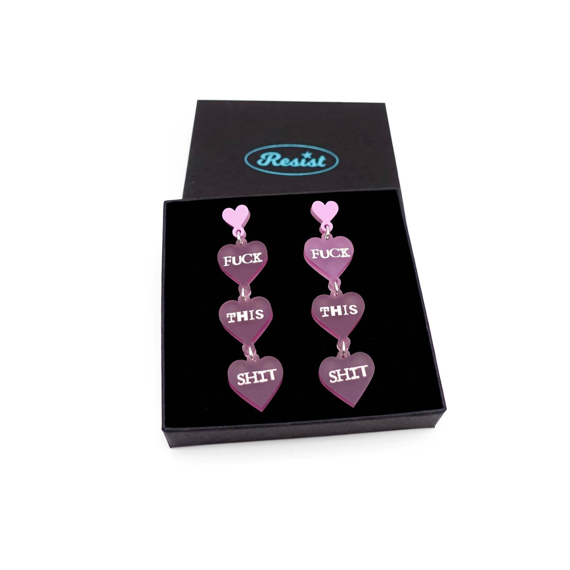 F*ck this Sh*t earrings in pale pink frost with glow-in-the-dark words shown in a Wear and Resist gift box.