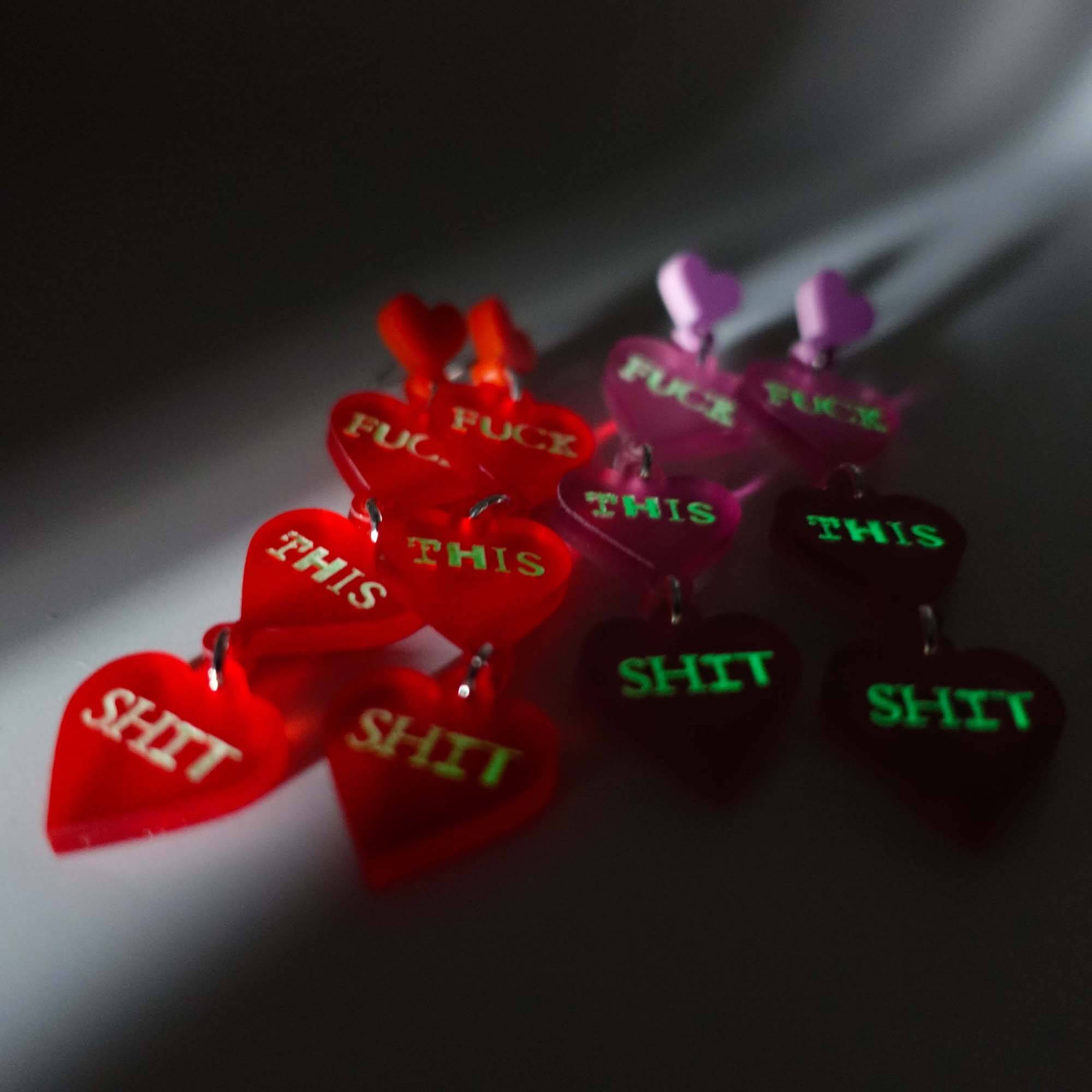 F*ck this Sh*t earrings in chilli red and pale pink, shown glowing in the dark.