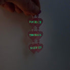 F*ck this Sh*t earrings in pale pink shown held up glowing in the dark.