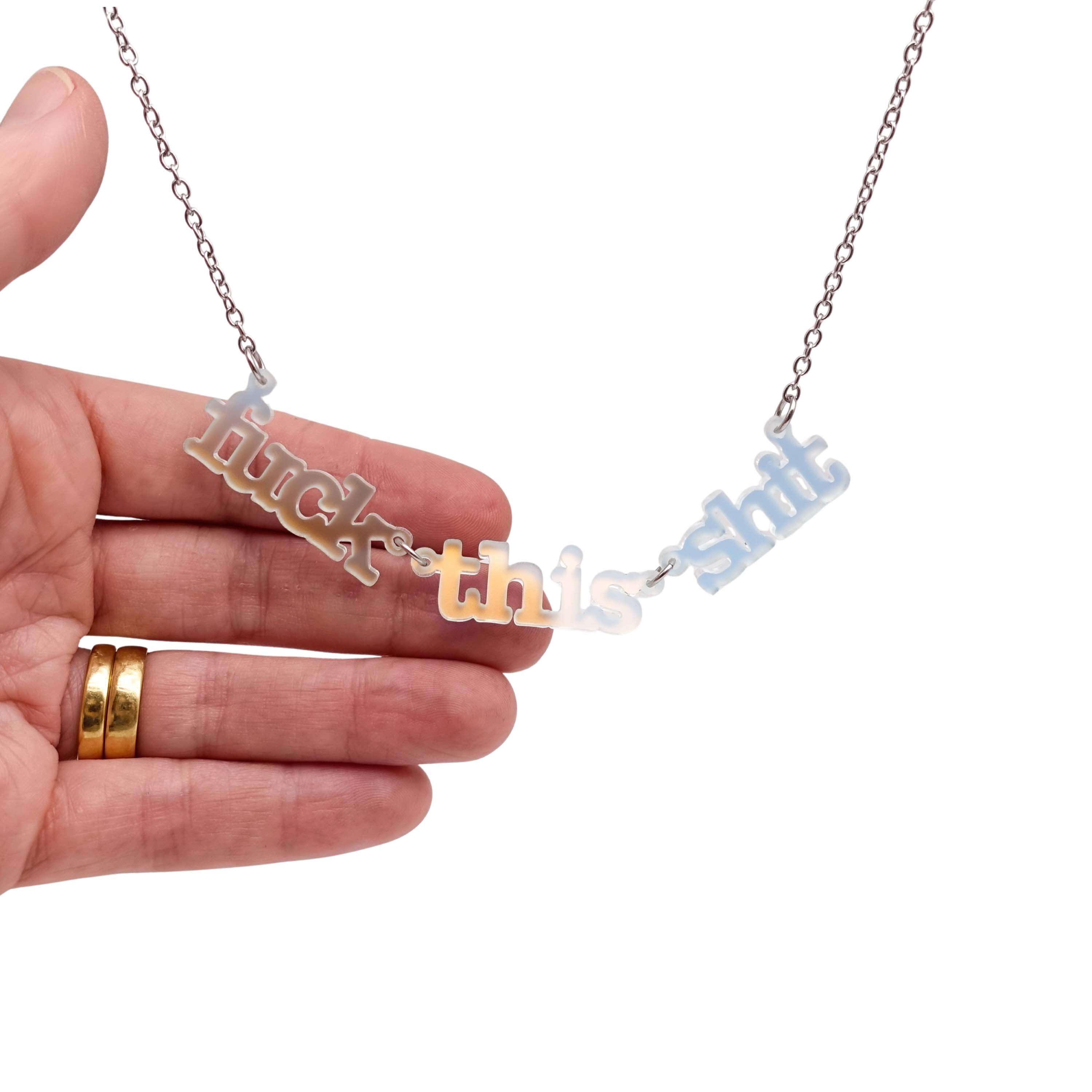 F*ck this Sh*t necklace in matte iridescent shown hanging on a stainless steel chain against a white background.