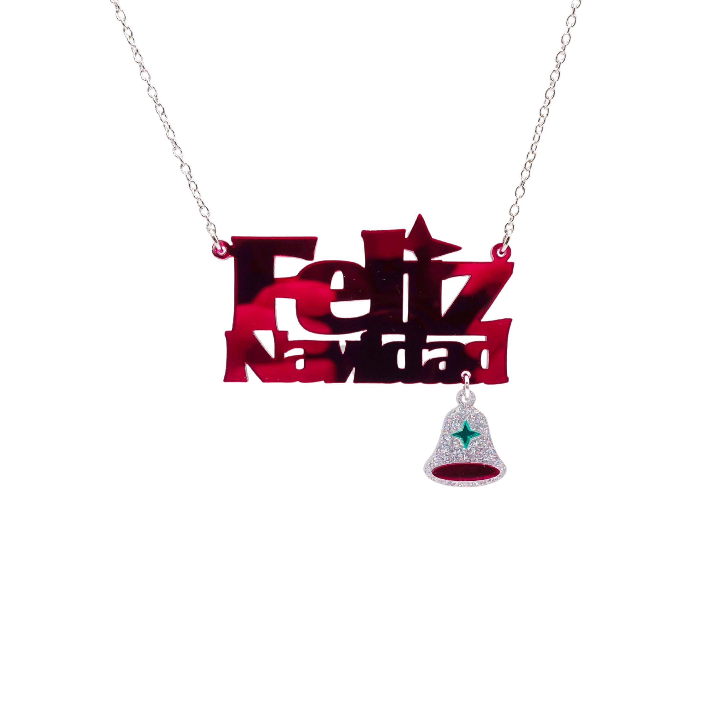 Feliz Navidad necklace in ruby mirror with a hanging glitter bell. Designed by Sarah Day for Wear and Resist.