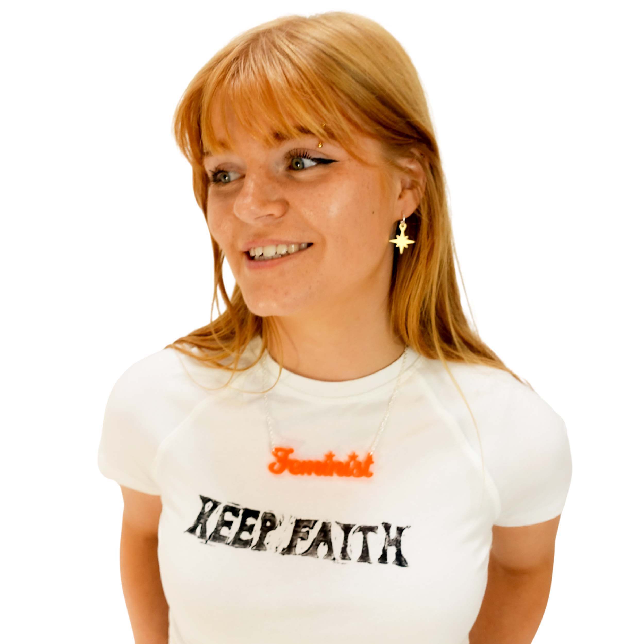 Eliza wears a script font Feminist necklace in fluoro orange with matte iridescent vintage star earrings.