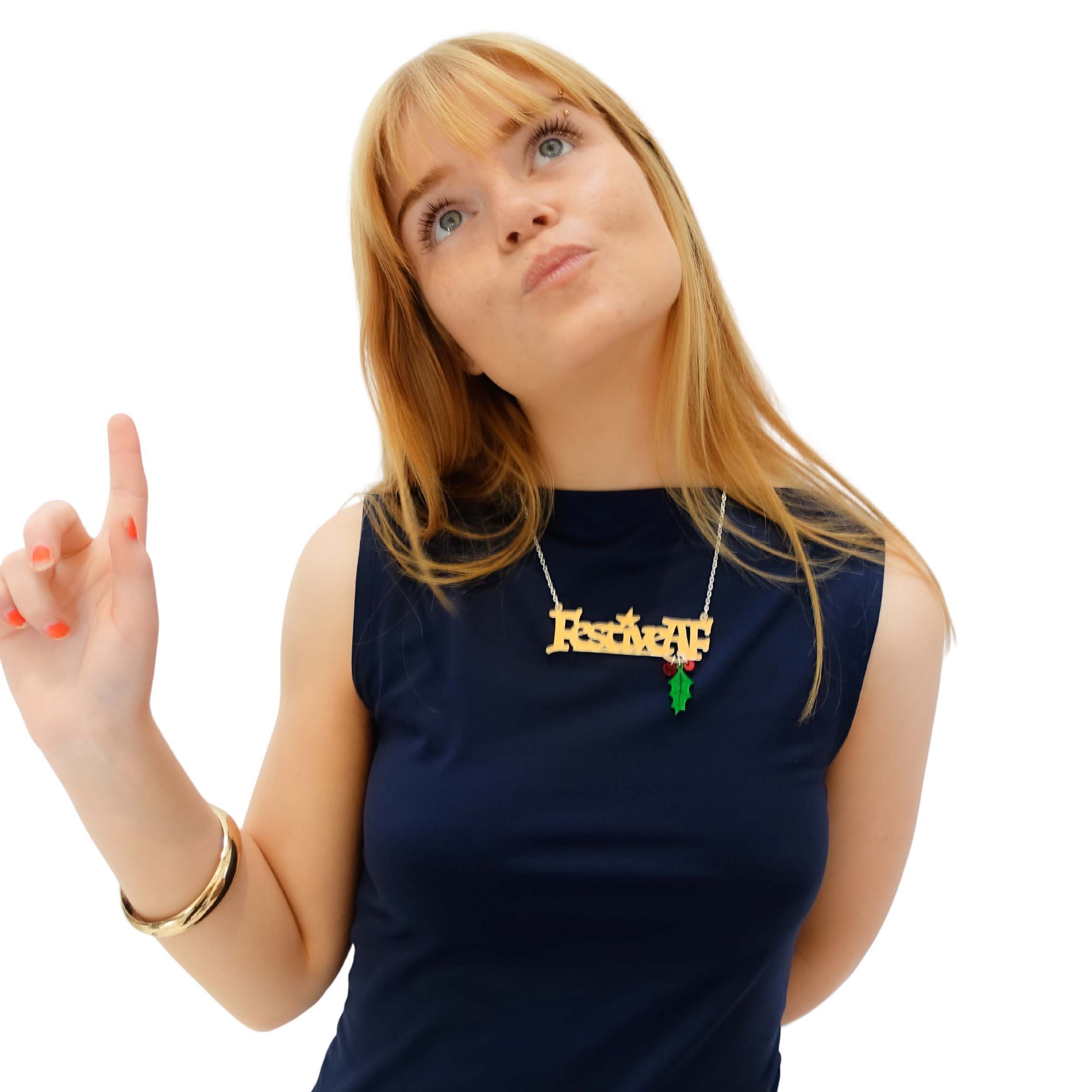 Eliza wears the Festive AF necklace in matte iridescent with dangling holly leaf and berries over a dark top.