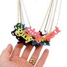 A group shot of the girly swot necklaces in all the retro colours hanging against a white background with my hand for scale.