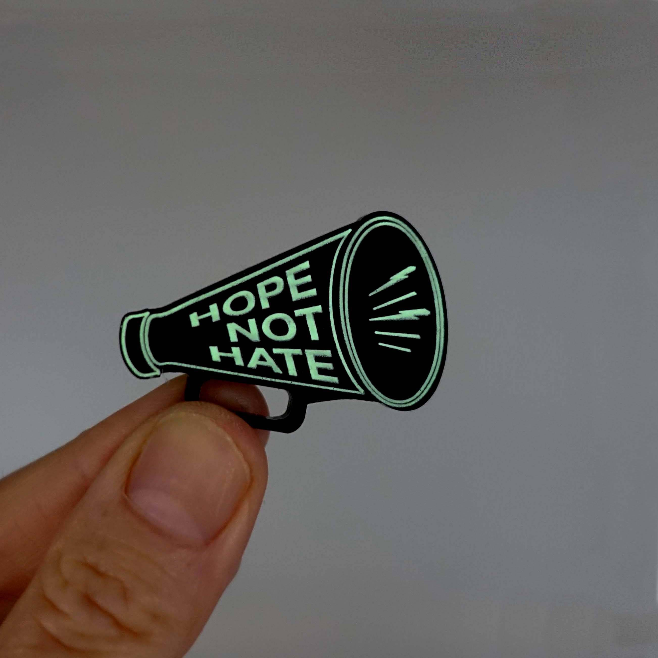 Megaphone brooch etched iwith the words Hope Not Hate, glowing in the dark.