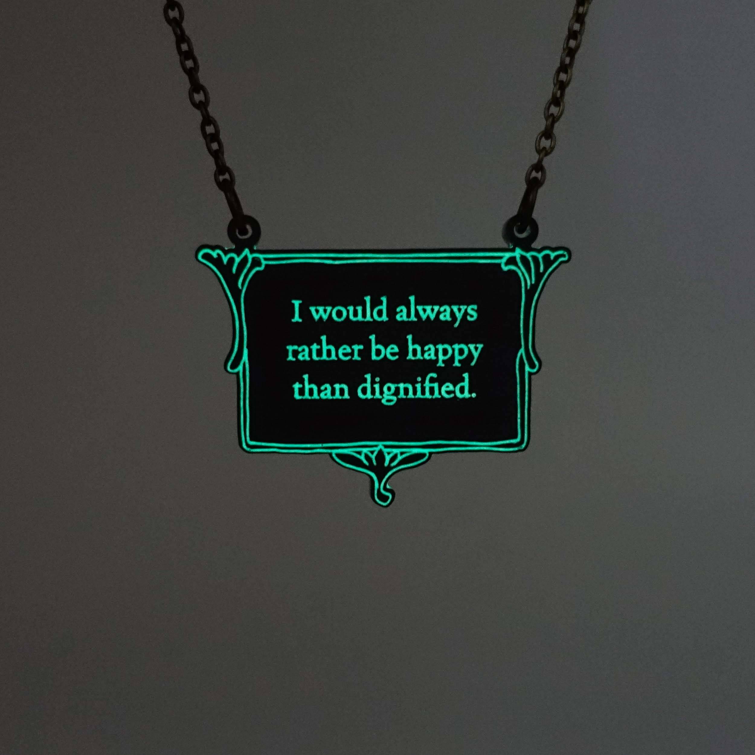 A vintage style slate necklace etched with the words of Jane Eyre 'I would always rather be happy than dignified', shown hanging on an antique gold chain glowing in the dark.