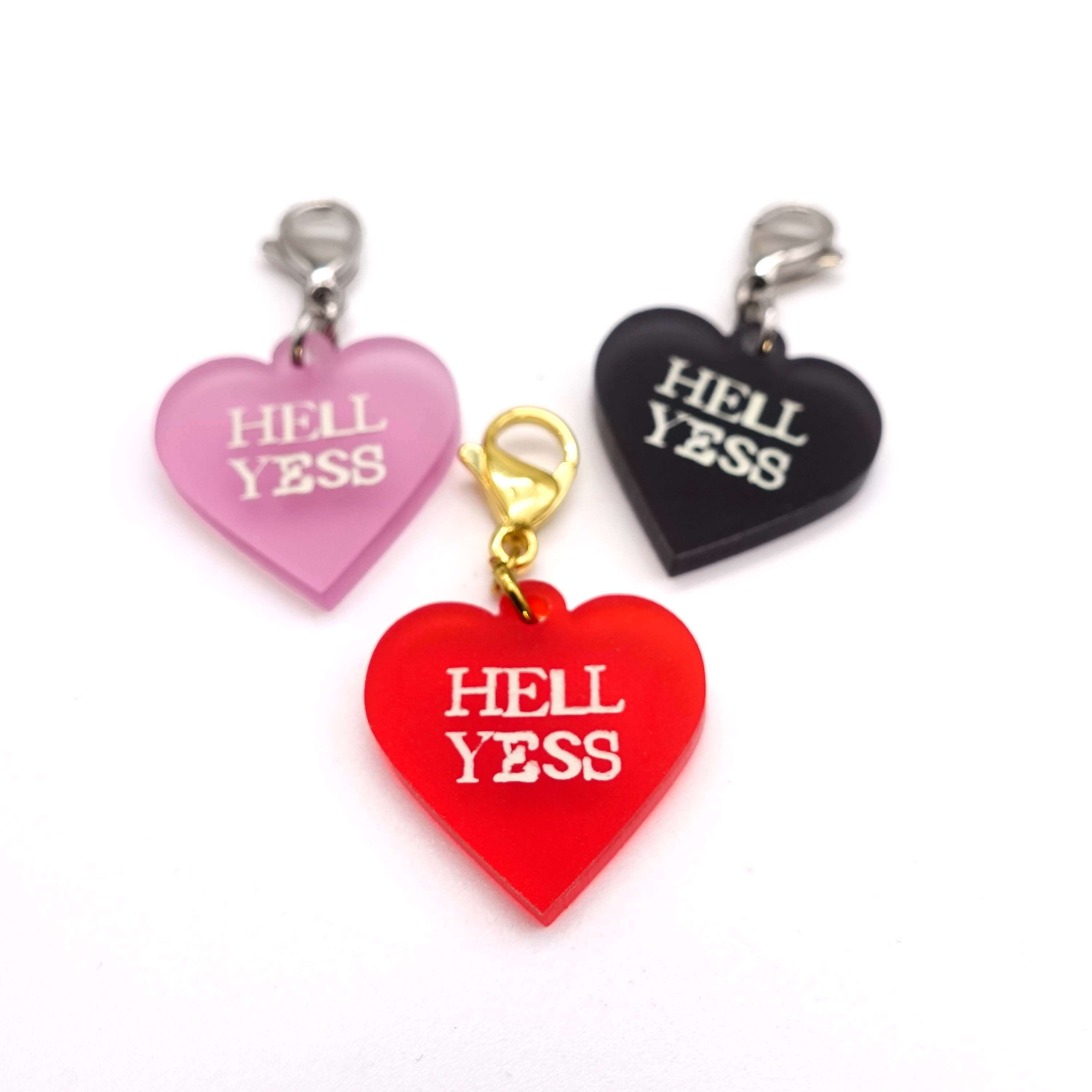Heart charms in chilli frost, pink frost and slate frost etched in glow-in-the-dark pigment with the words 'Hell Yess'