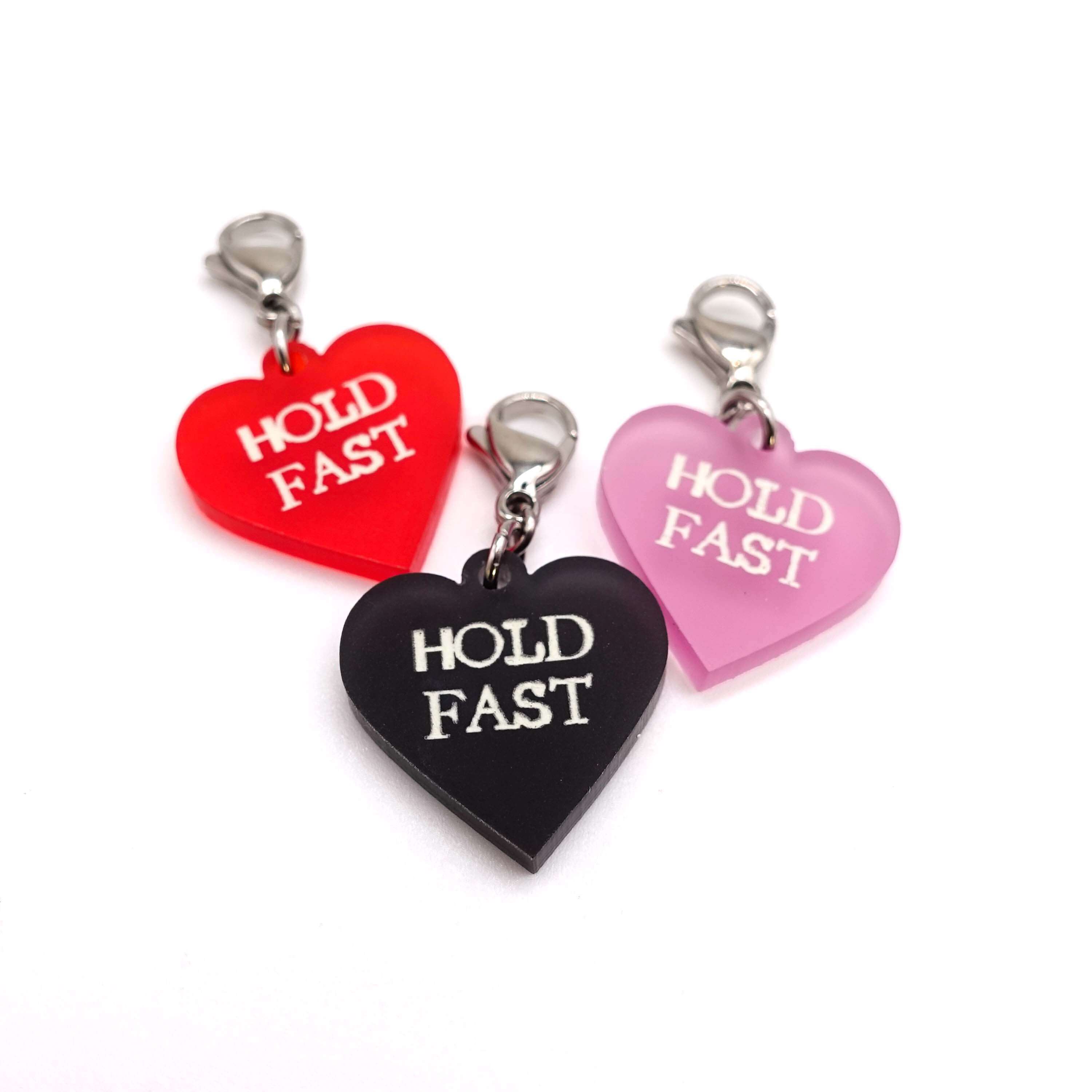 Heart charms in chilli frost, pink frost and slate frost etched in glow-in-the-dark pigment with the words 'Hold Fast'