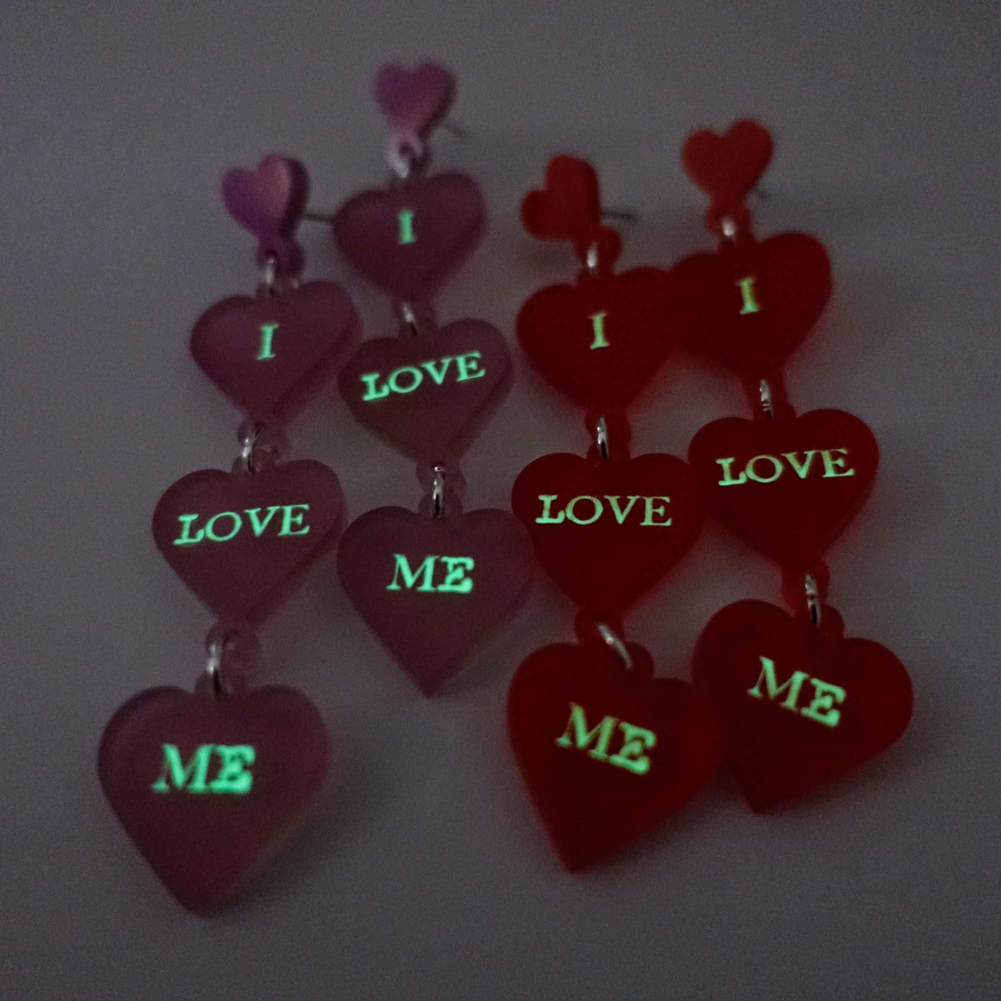 I Love Me heart drop earrings shown glowing in the dark.