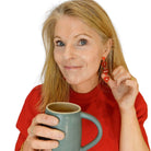 Sarah holds a cup of tea and wears red I love Me earrings in red.