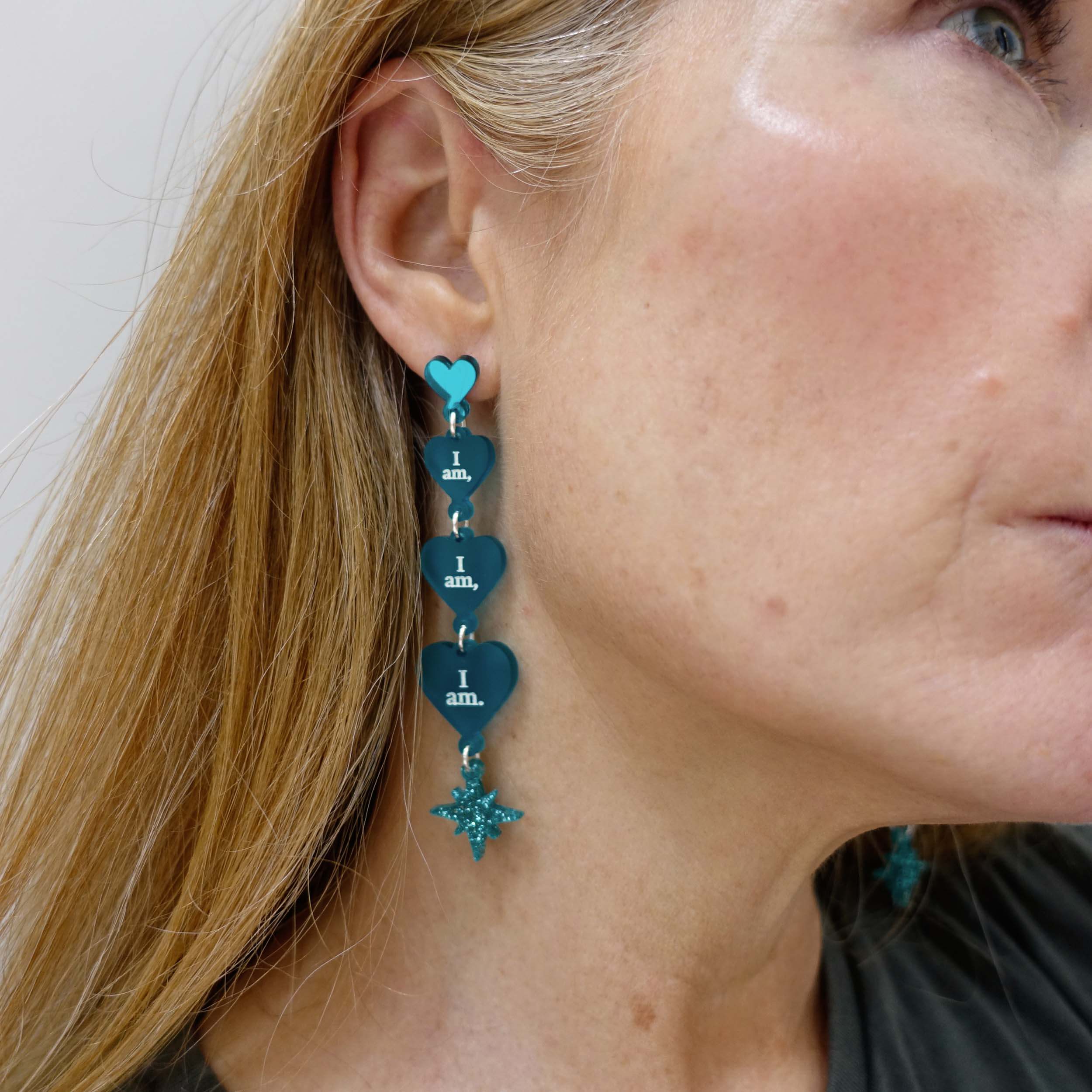 Sarah Day, founder of Wear and Resist wears teal frost  I am I am I am heart drop earrings.