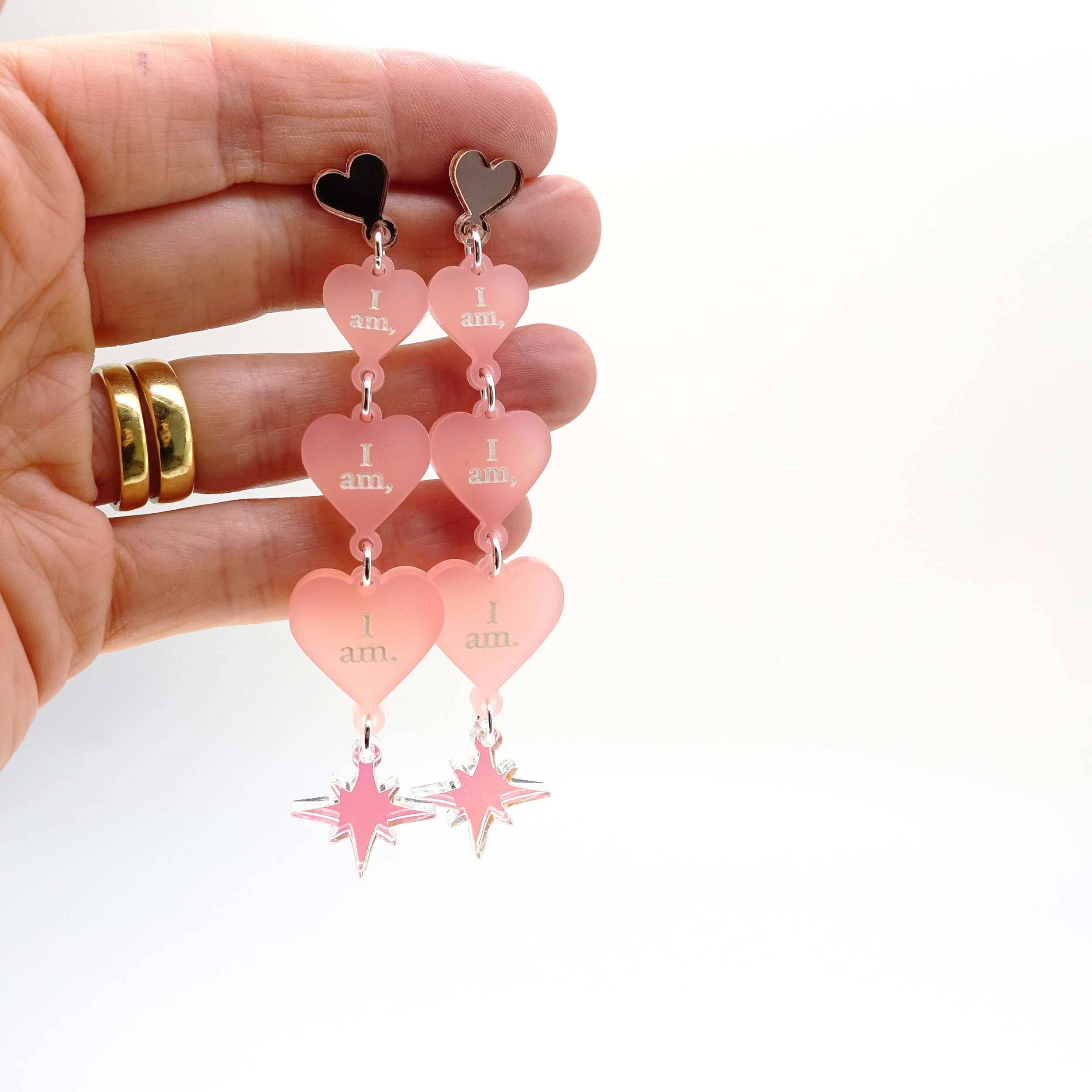 Blush frost  I am I am I am heart drop earrings shown held up for scale.