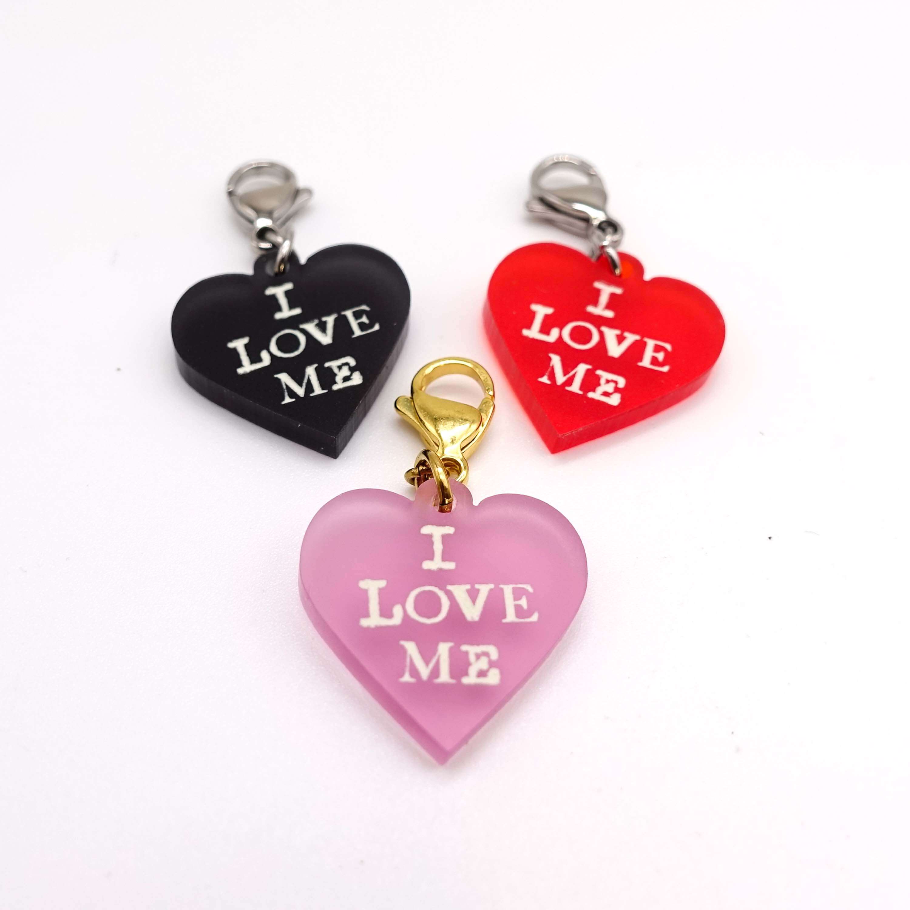 Heart charms in chilli frost, pink frost and slate frost etched in glow-in-the-dark pigment with the words 'I love me'