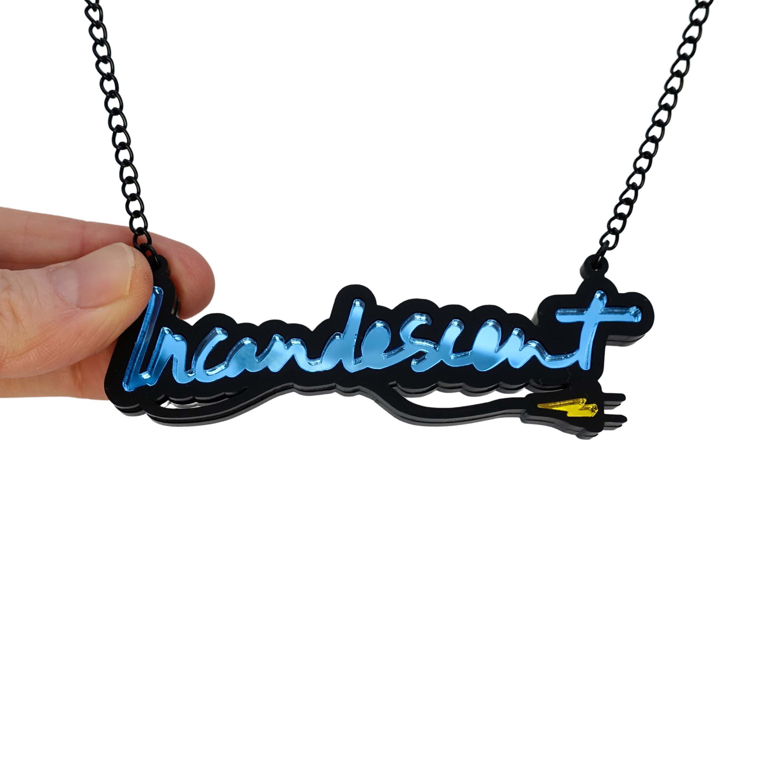 Incandescent neon necklace in sky blue with a yellow lightning bolt plug, on a black chain adjustable to three lengths. Shown hanging against a white backround with my hand holding it for scale.