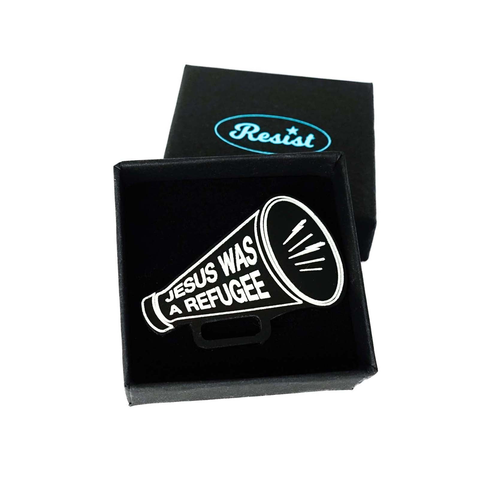Black megaphone brooch etched in glow-in-the-dark paint with the words Jesus was a Refugee. Shown in a small Wear and Resist gift box.