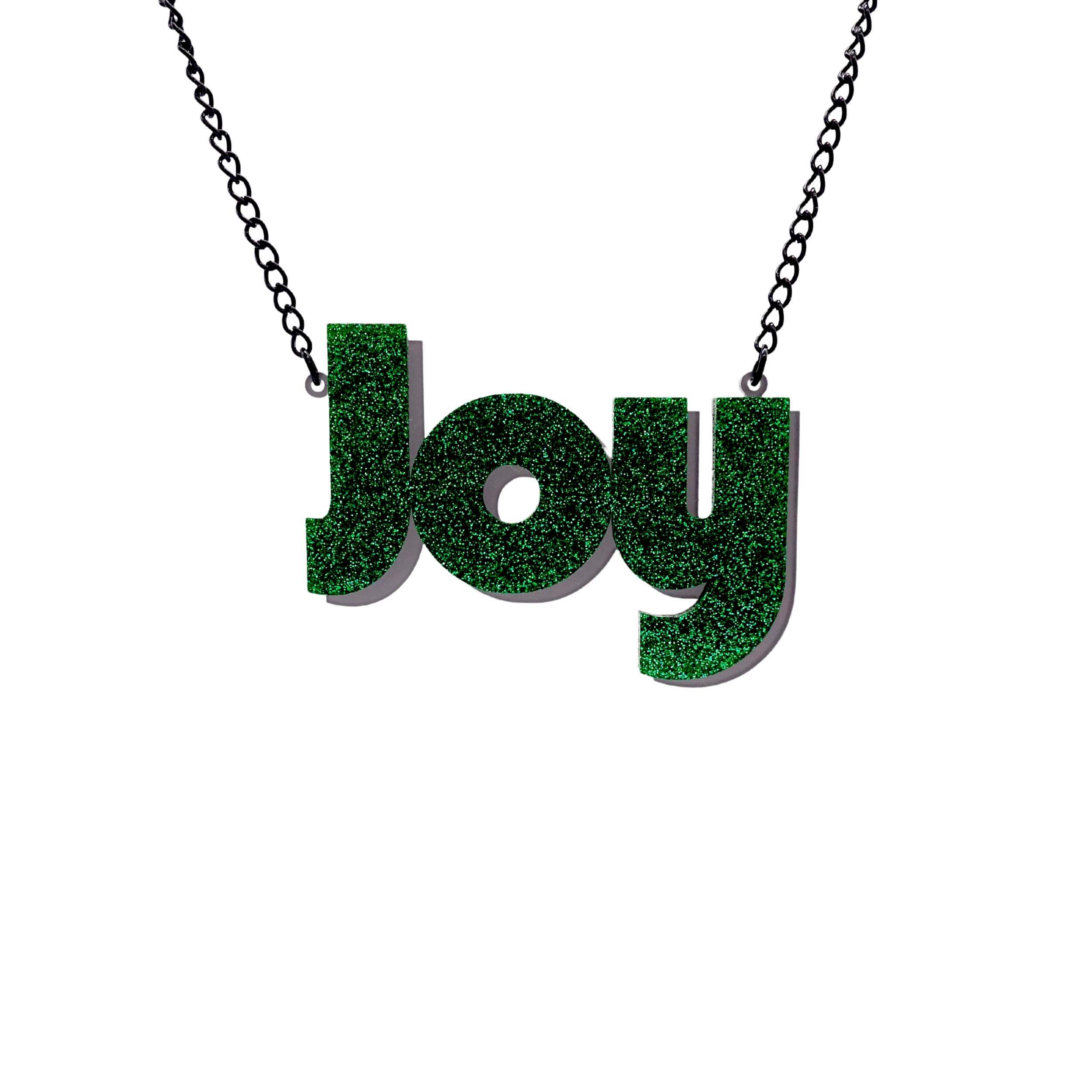Joy statement necklace in green glitter, with slate frost drop shadow backing layer. Shown hanging against a white background.
