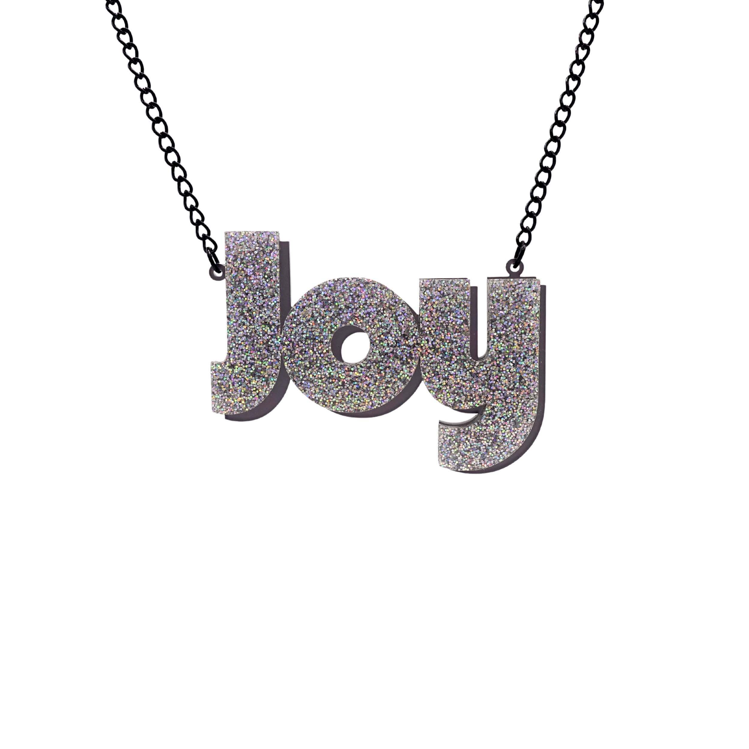 Joy statement necklace in silver glitter, with slate frost drop shadow backing layer. Shown hanging against a white background.