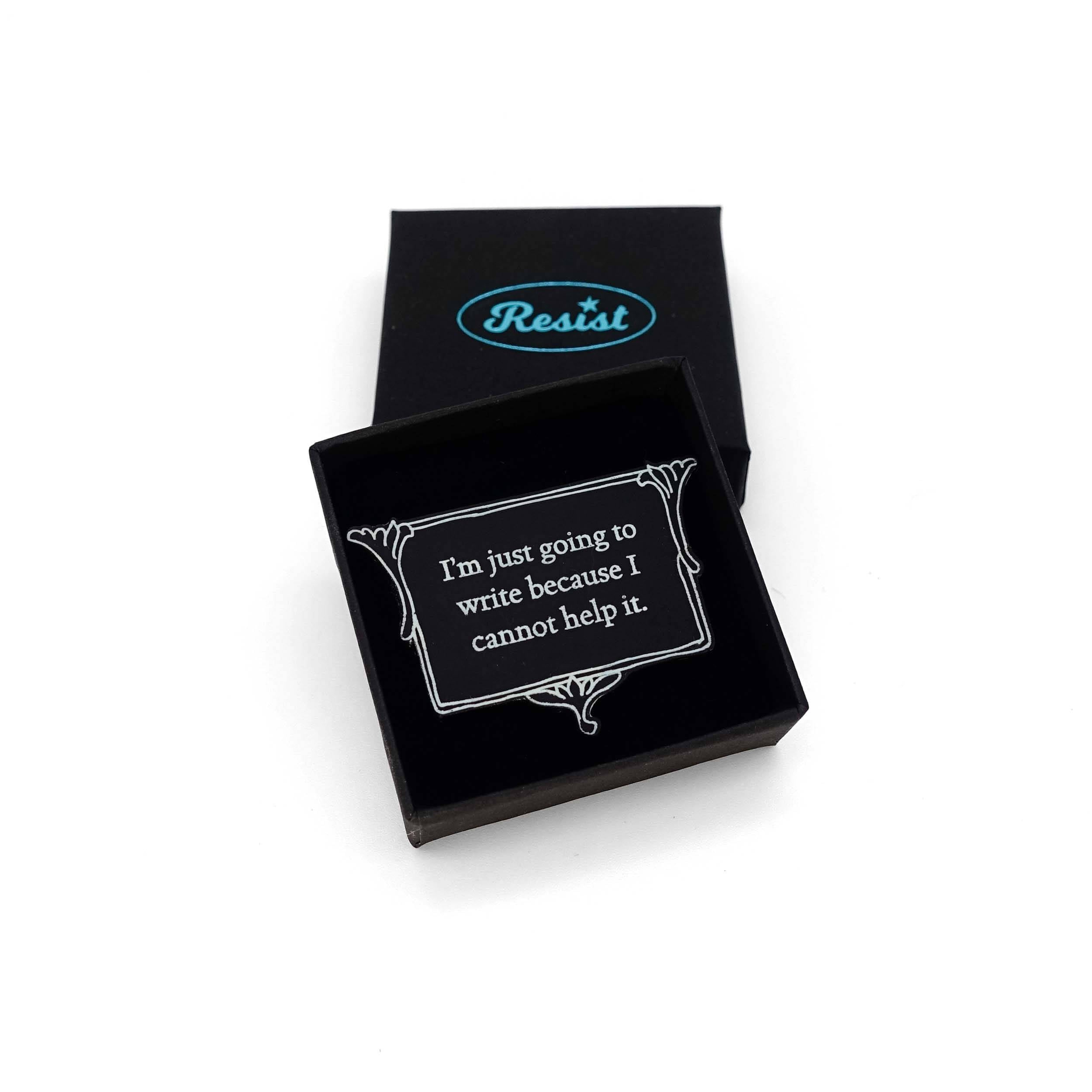 A vintage style black and white brooch etched in glow-in-the-dark pigment with Charlotte Bronte's words: 'I'm just going to write because I cannot help it,' shown in a small Wear and Resist gift box.