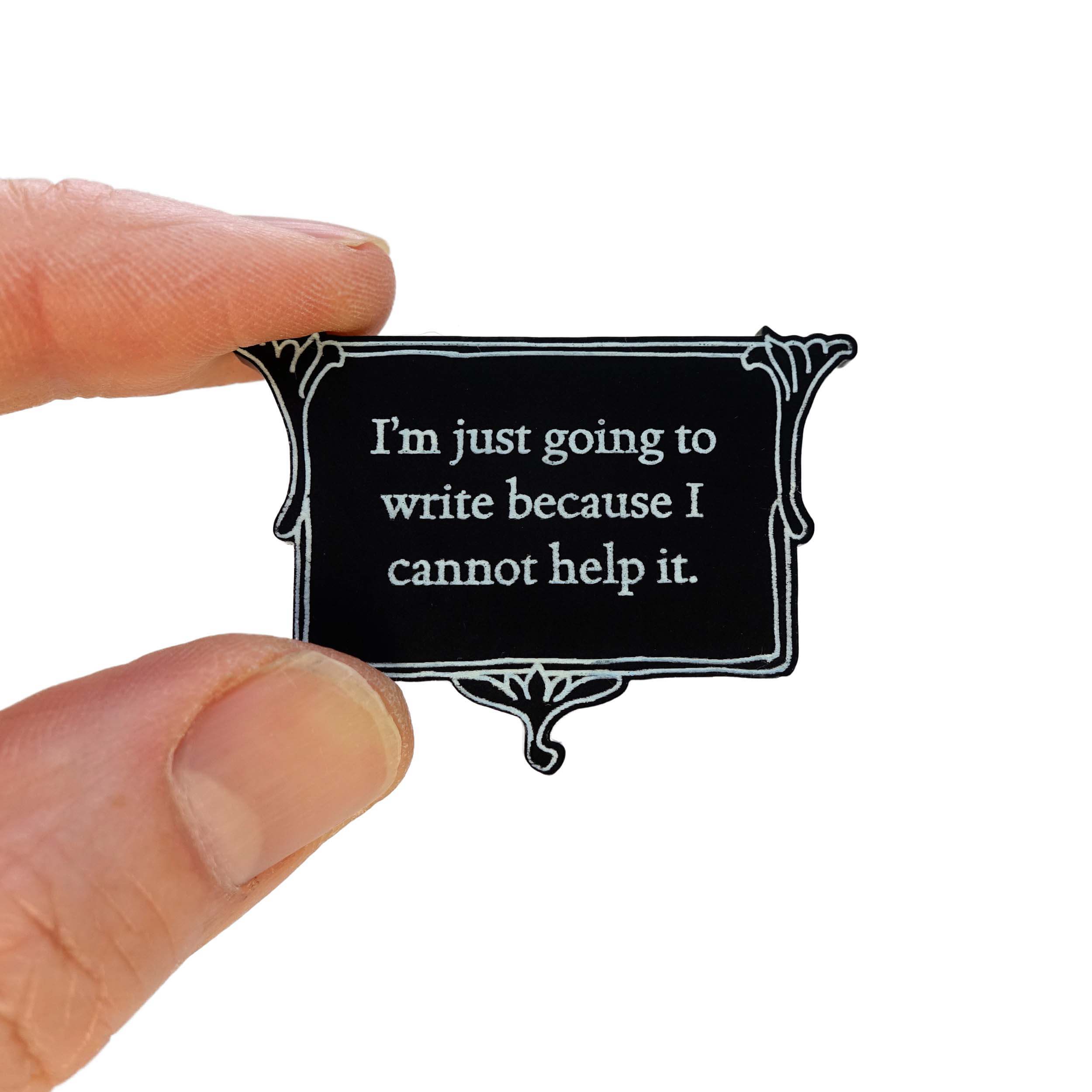 A vintage style black and white brooch etched in glow-in-the-dark pigment with Charlotte Bronte's words: 'I'm just going to write because I cannot help it,' shown held up in my fingers for scale.