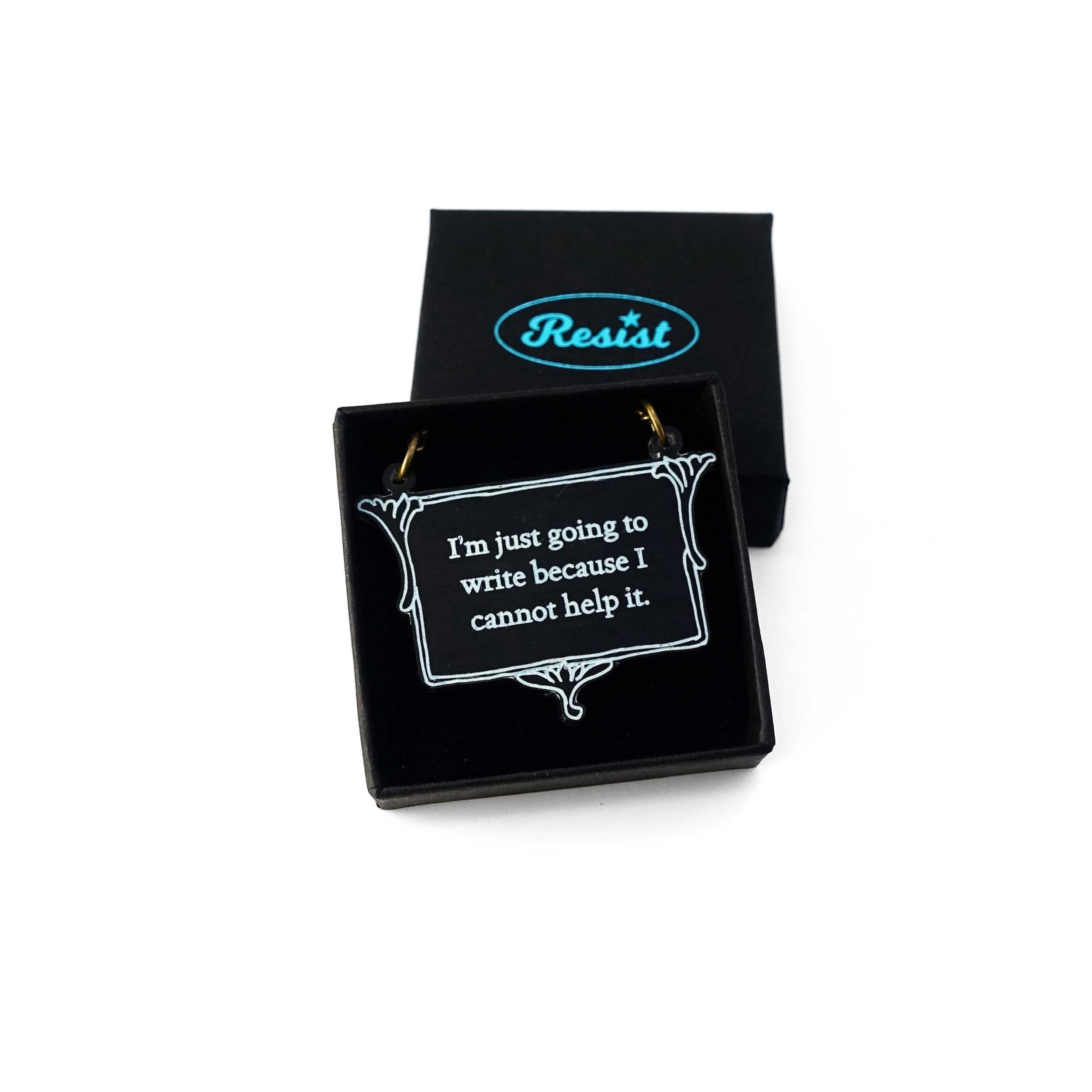 A vintage style slate frost necklace etched with Charlotte Brontë's words in glow-in-the-dark pigment that says, 'I'm just going to write because I cannot help it.' It is shown in a small Wear and Resist gift box.