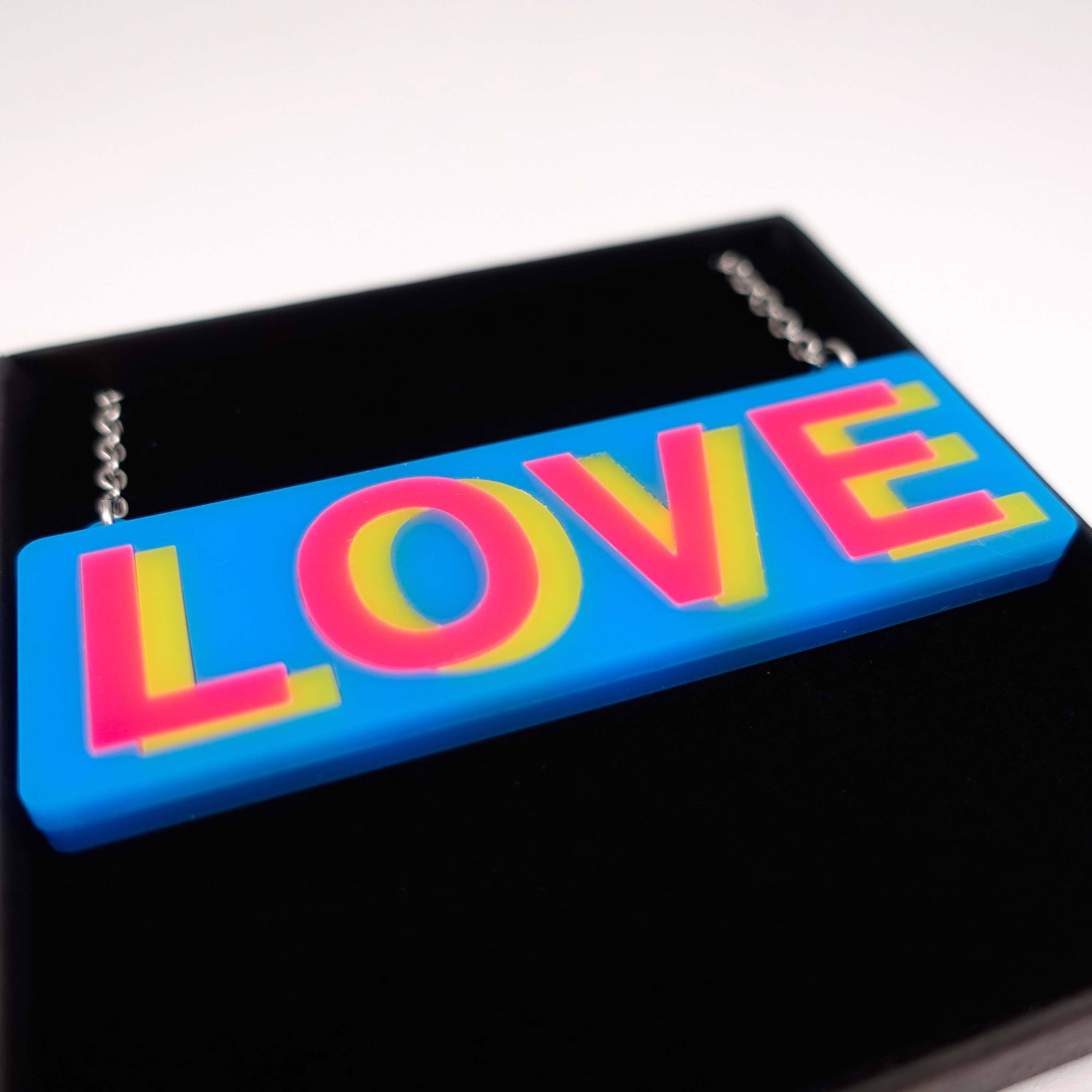 A close up of the LOVE necklace in colourful blue, hot pink and yellow, shown in a Wear and Resist gift box.