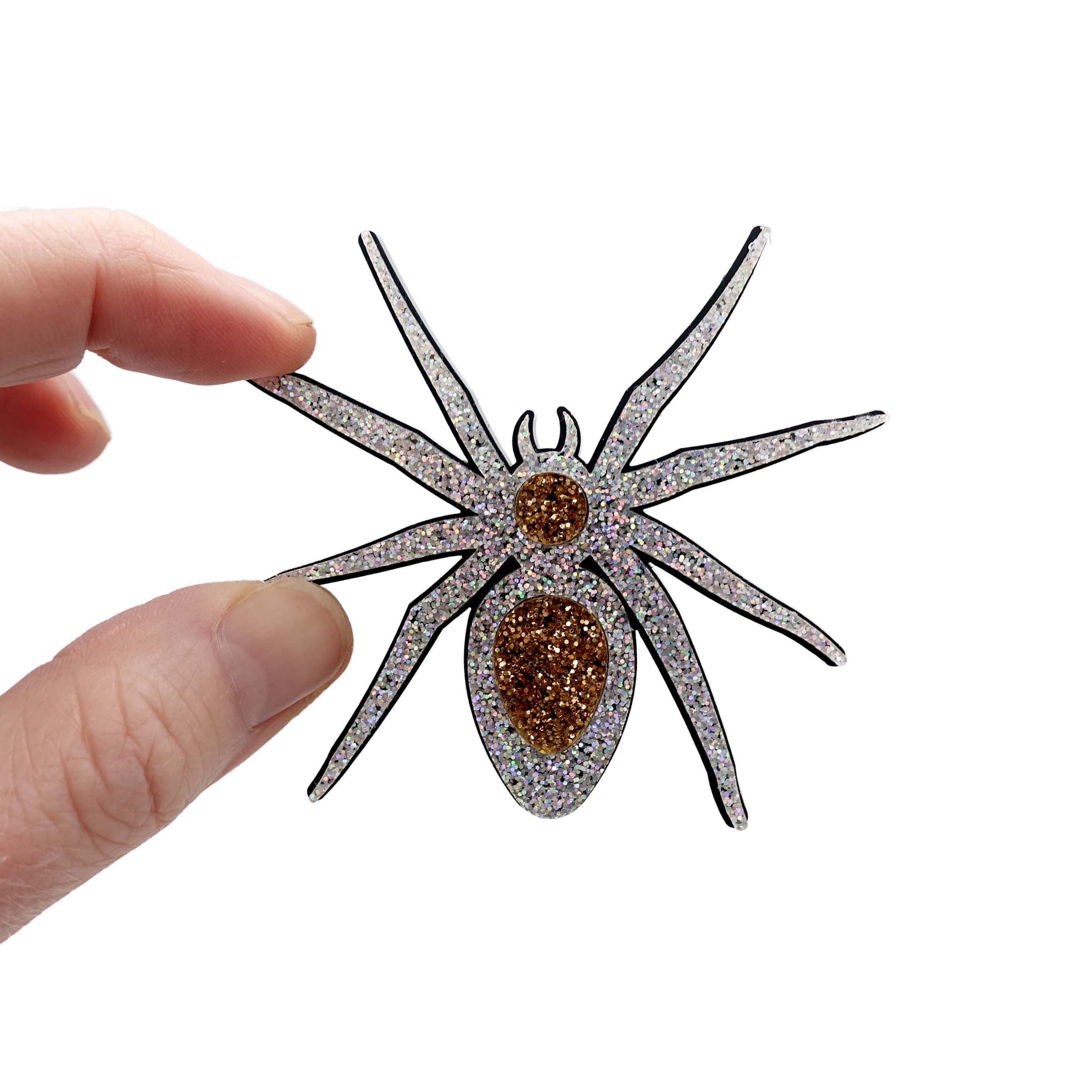 Sarah's fingers hold up the All Hail Lady Hail Spider brooch against a white background.