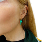 Sarah wears small electric green lightning bolt hoop earrings on gold plated hoops.