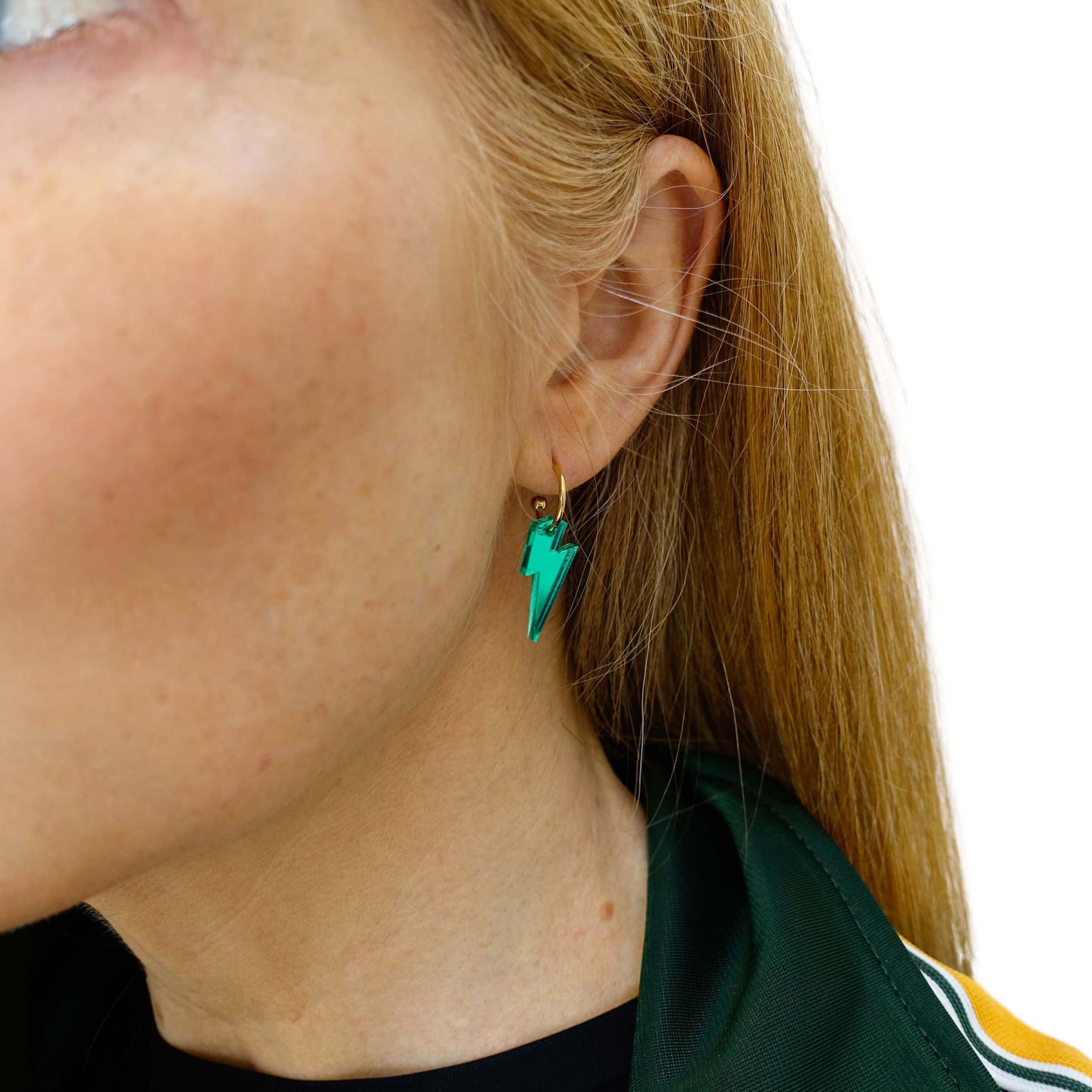 Sarah wears small electric green lightning bolt hoop earrings on gold plated hoops.