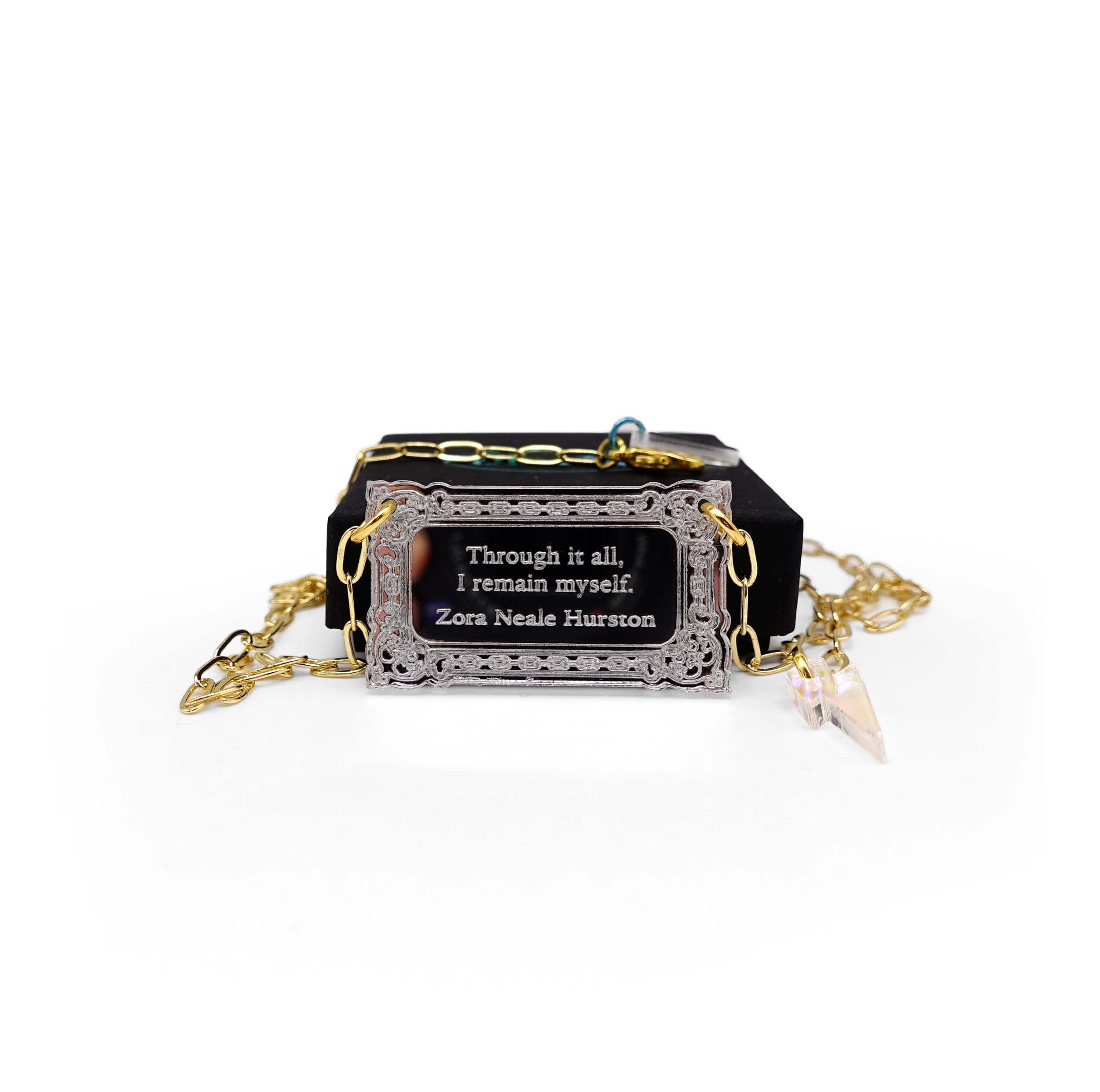 Literary Quote necklace etched with a quote by Zora Neale Hurston, 'Through it all, I am myself.' Shown on a gold plated paperclip chain in front of a small Wear and Resist gift box.