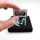 Literary Quote necklace etched with a quote by Audre Lorde, 'I am deliberate and afraid of nothing.' Shown held up in my hand for scale in front of a small Wear and Resist gift box.